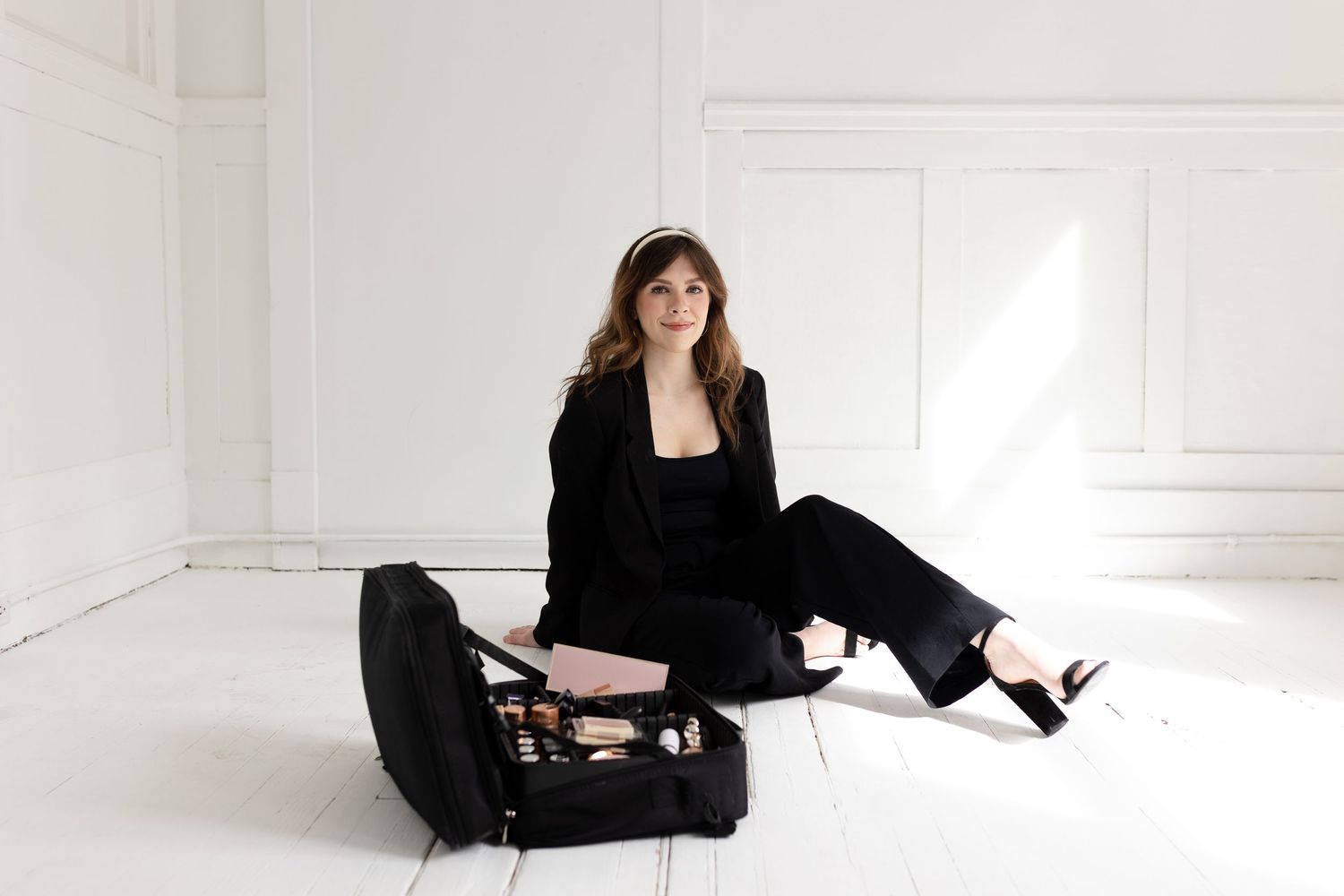 Fashion portrait with instrument case in all-black outfit against white studio background.