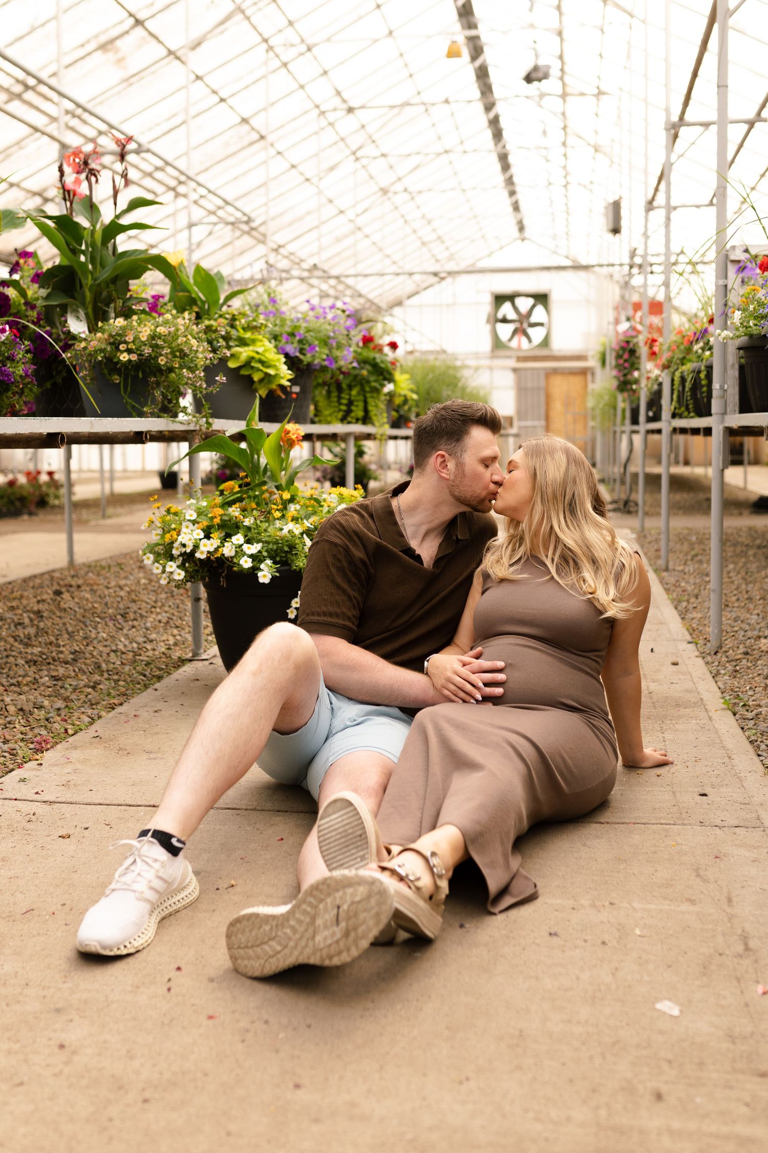 Couple lounging on greenhouse floor surrounded by potted flowers and plants.