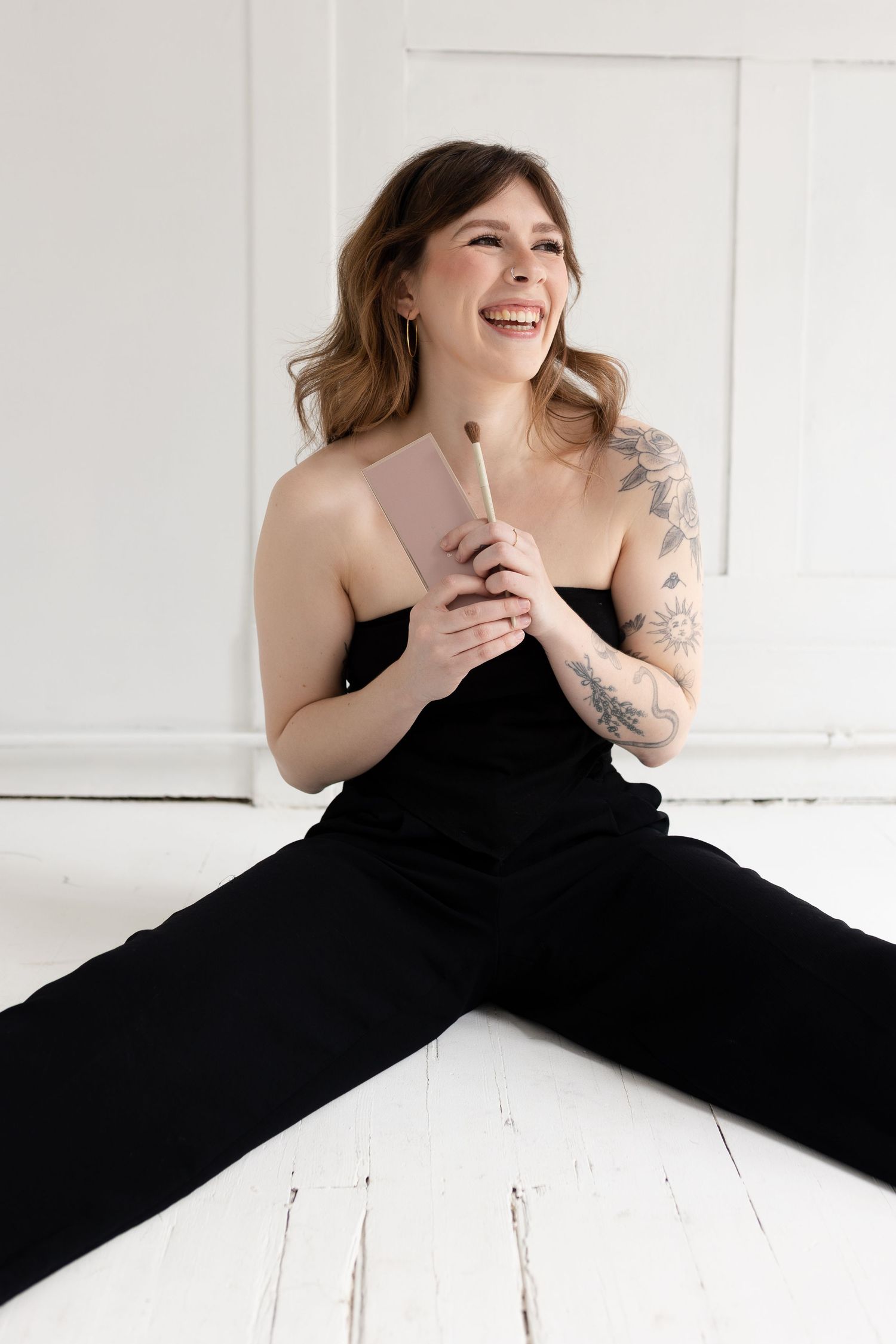 A person in black attire doing splits on a white floor with visible tattoos.
