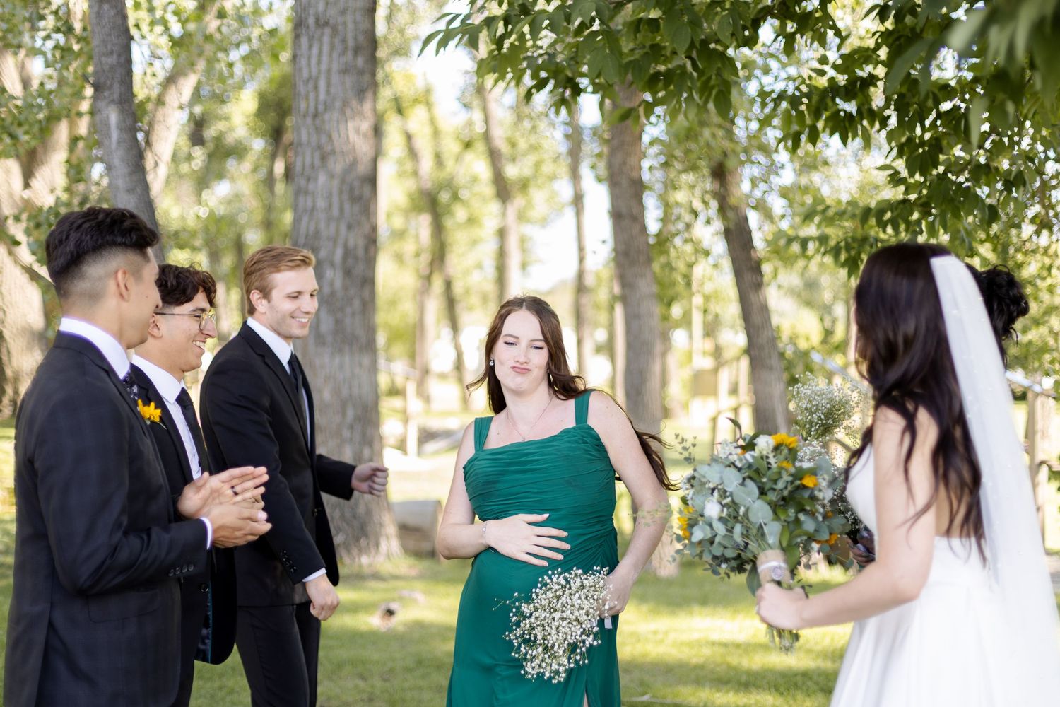 Wedding party members in formal attire share a candid moment during outdoor photo session.