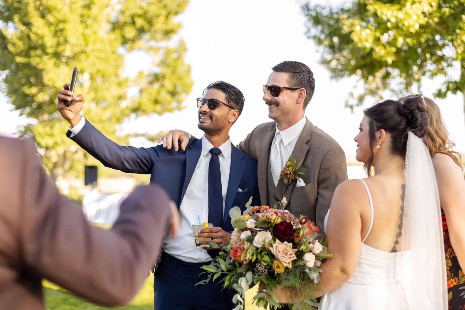 Wedding party members in formal attire gather outdoors for candid moments during a sunny celebration.