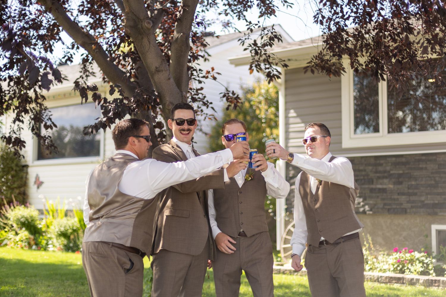 Groomsmen in brown suits sharing laughs outdoors under trees.