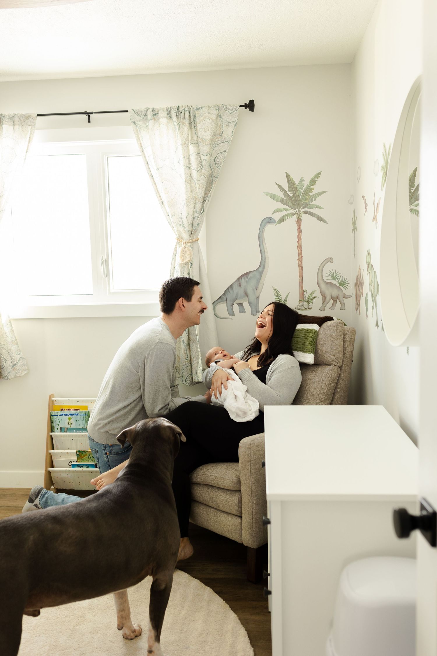 A tender family moment captured in a nursery decorated with palm tree wall art and a cozy gray couch.