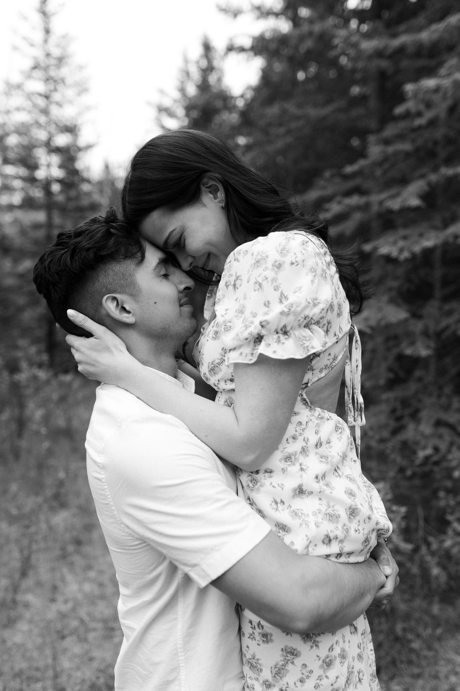 An intimate black and white portrait of a couple embracing in a forest setting.