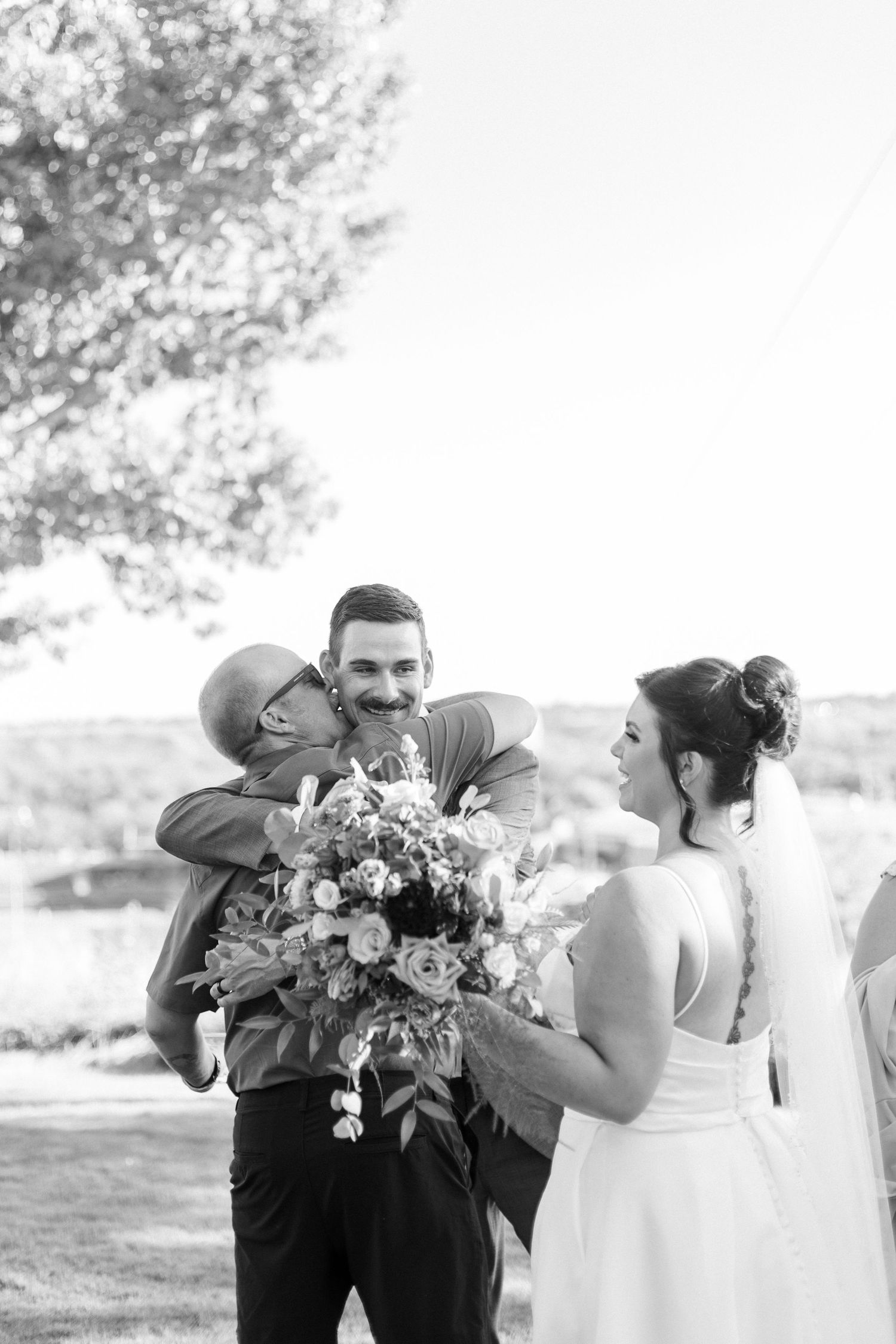Wedding party sharing emotional embraces outdoors in black and white photography.