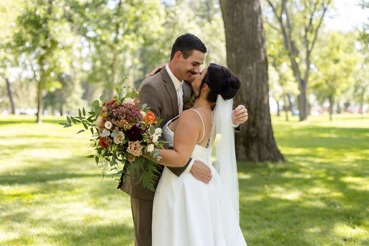 Couple embracing in a sunny park setting during their wedding day.