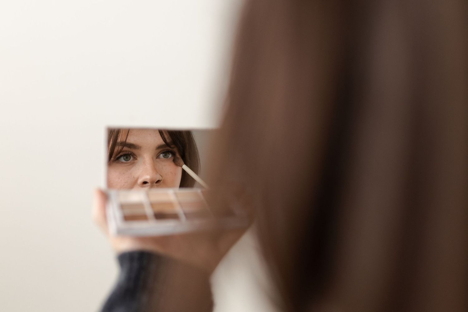 A blurred reflection in a broken mirror shows fragments of someone looking through shattered glass pieces.
