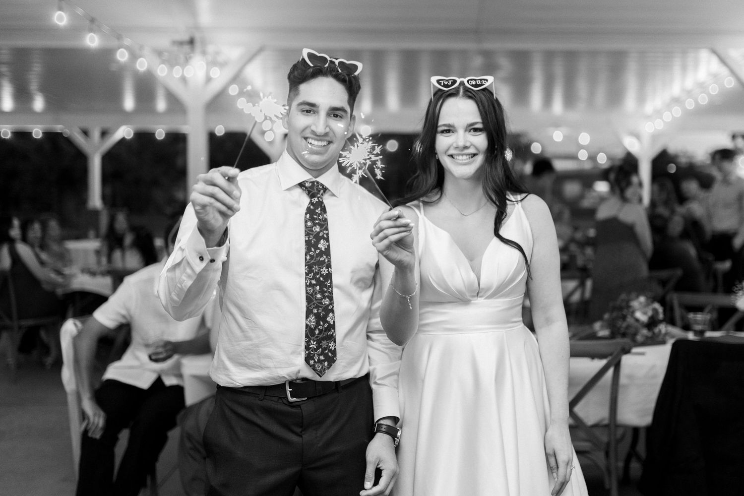 Wedding reception guests dance and celebrate under a white tent with string lights.