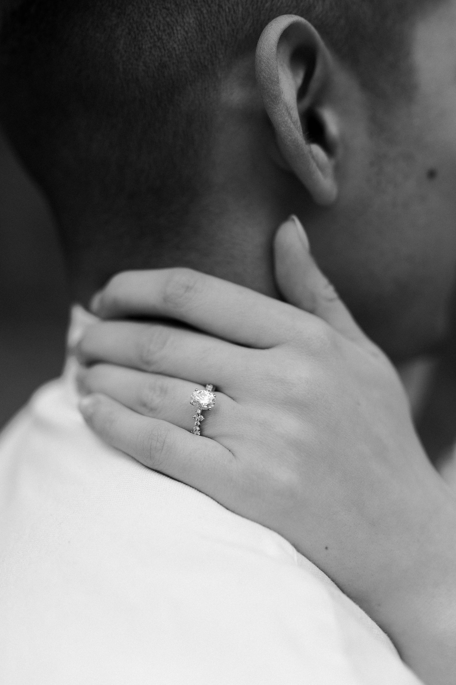 Close-up black and white photo of an engagement ring and embrace.