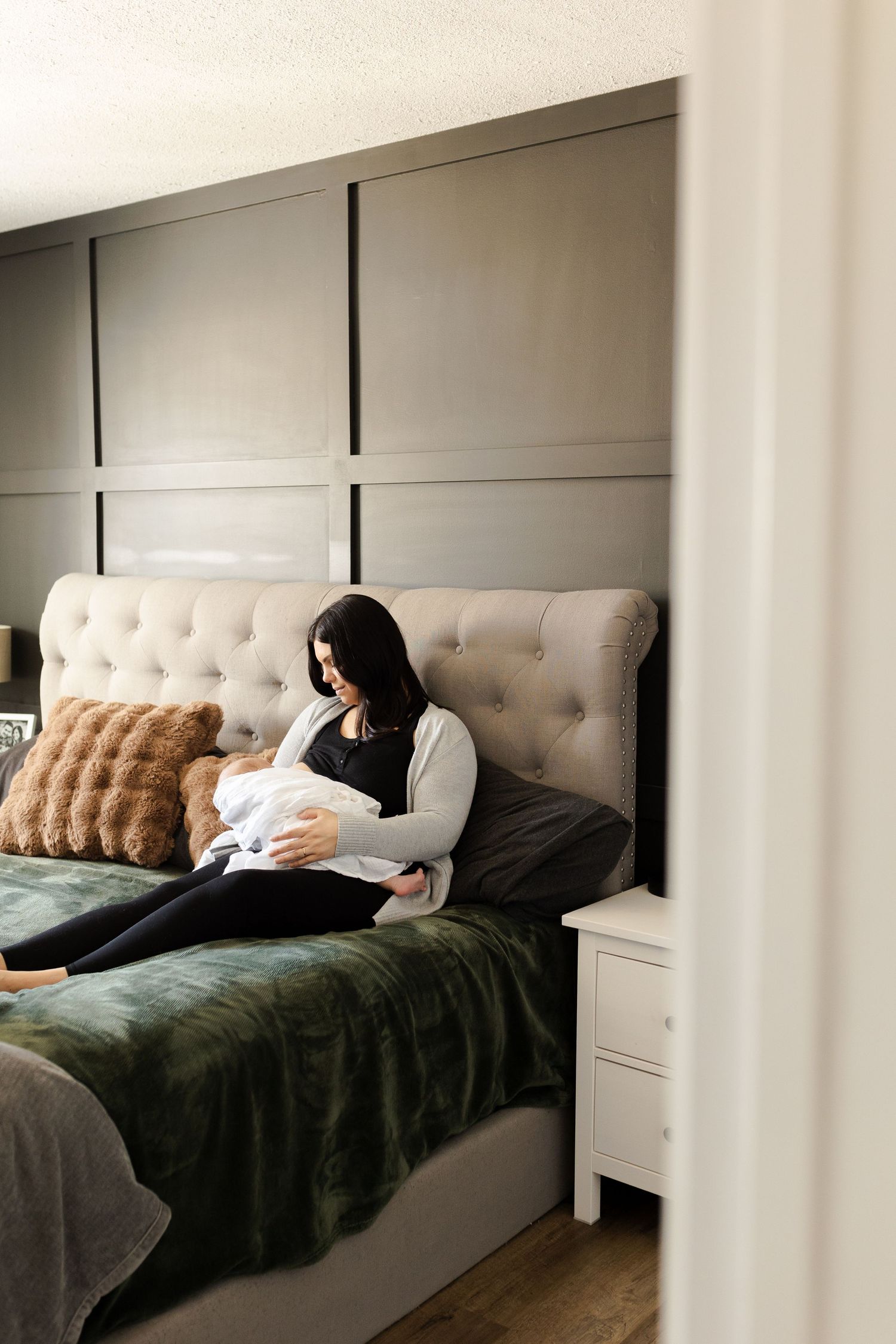 Modern bedroom interior with gray bedding and tufted headboard during intimate family time.
