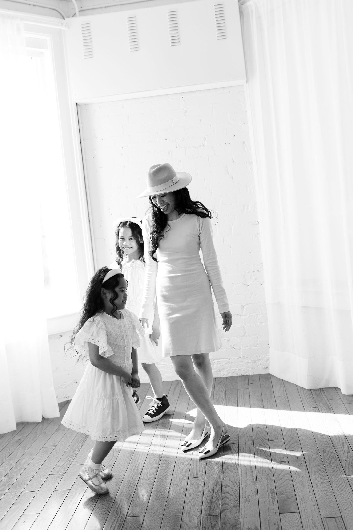 Black and white photo of figures in white dresses creating playful shadows on wooden floor.