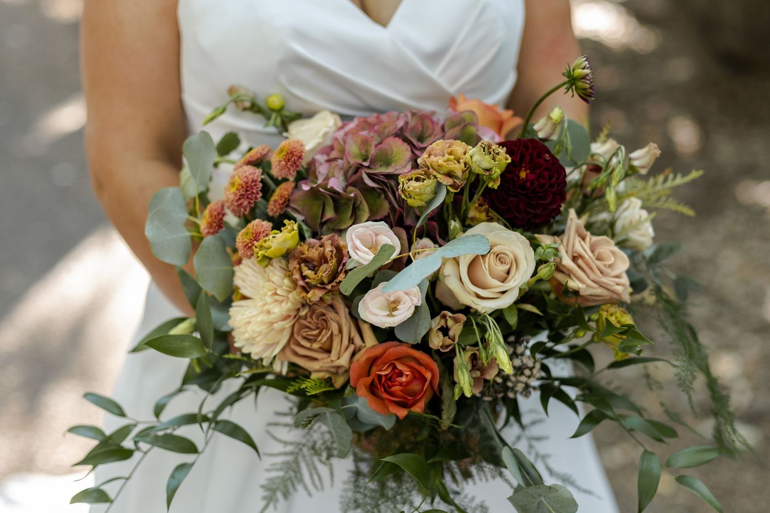 Close-up of elegant bridal bouquet with roses and mixed flowers in muted fall colors.