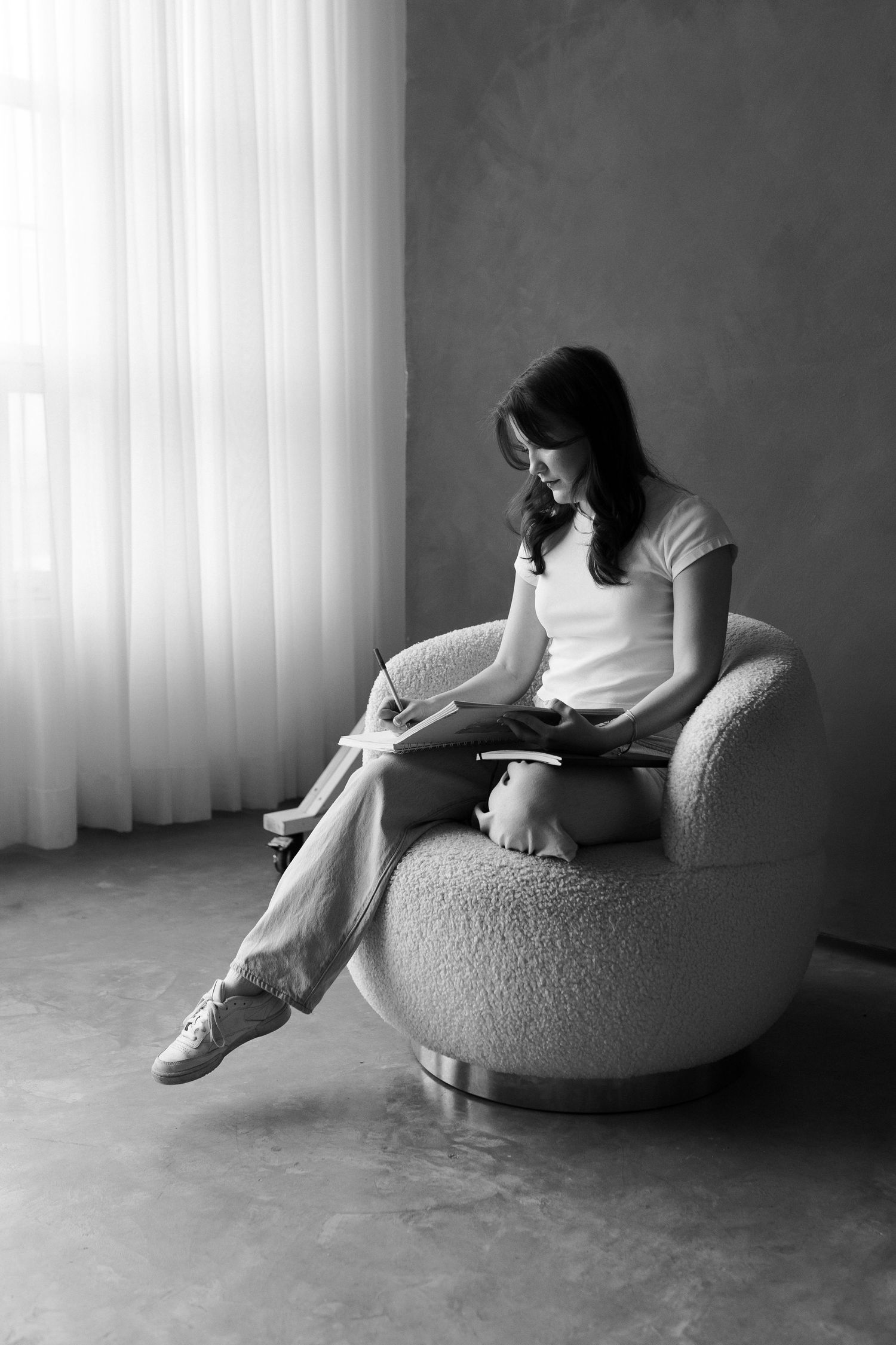 Black and white photo series showing a person writing in a notebook while sitting on a round chair.