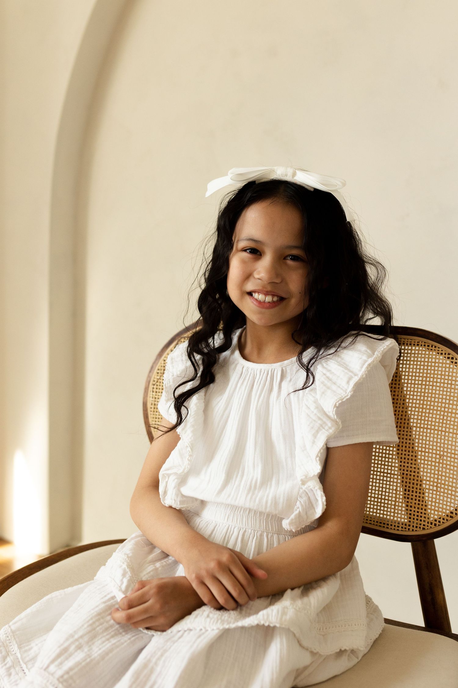 Candid portraits on a cane chair showing joyful expressions in white summer dresses.