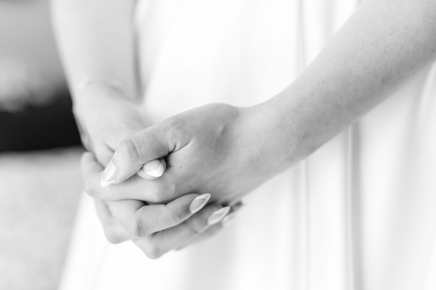 Close-up black and white photo of clasped hands in prayer or meditation against a light background.