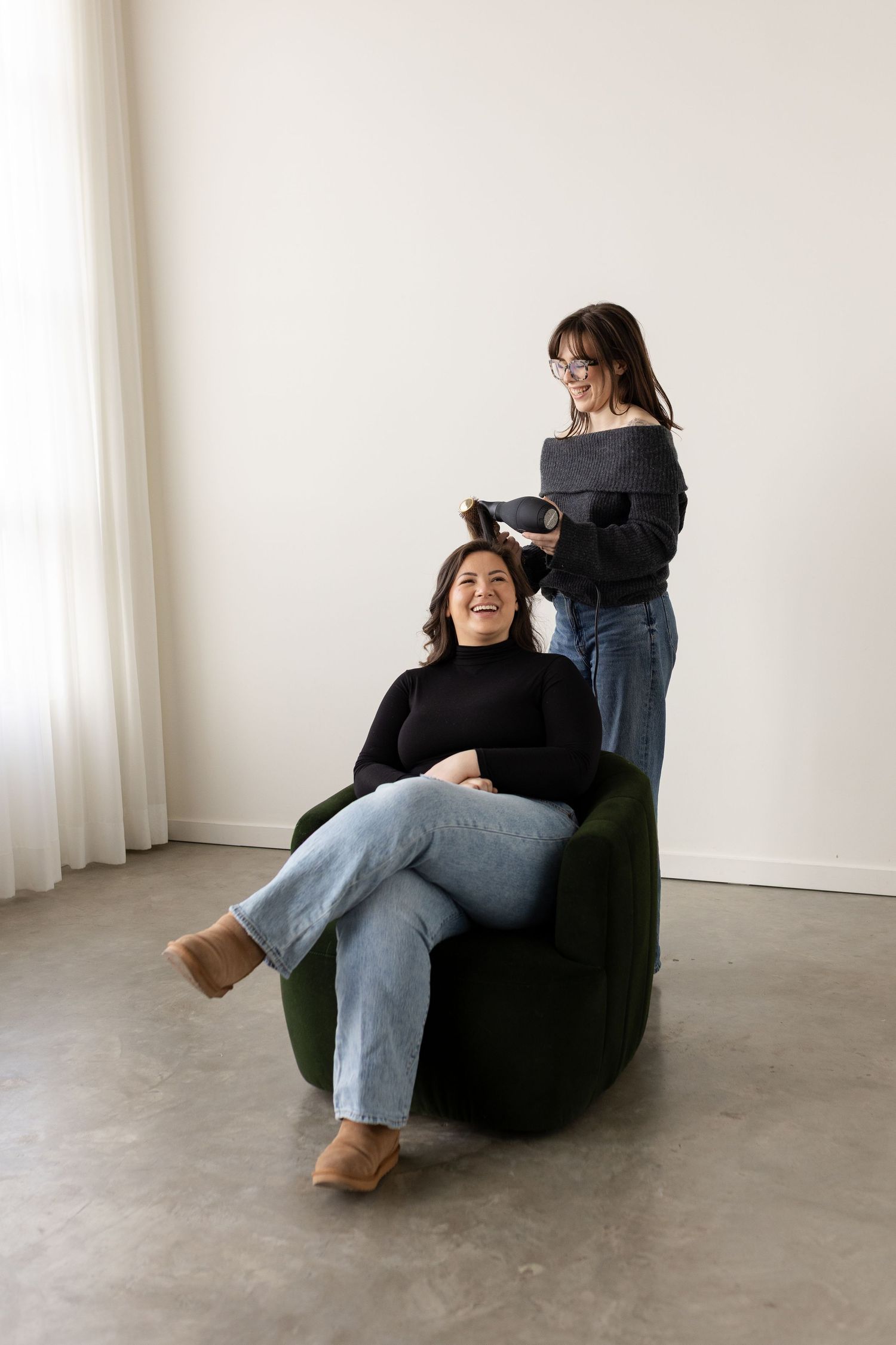 Two people in black sweaters and jeans during a casual photo session in a minimalist white room setting.