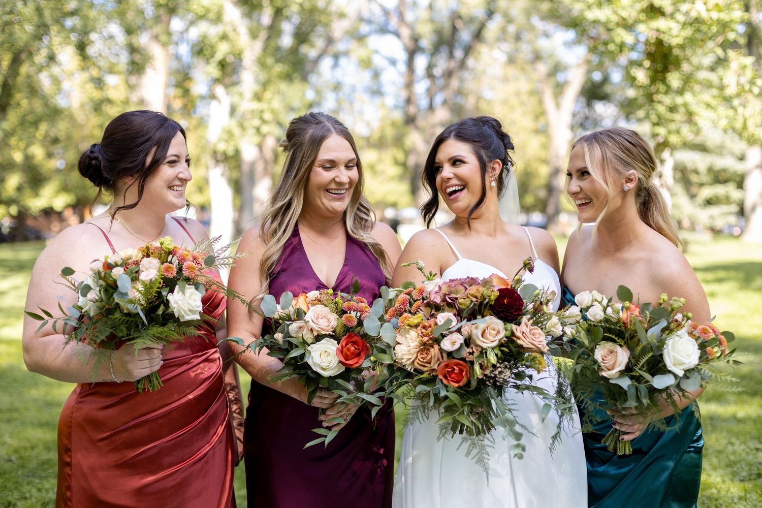 Bridesmaids in burgundy dresses pose with bouquets alongside the bride in an outdoor setting.