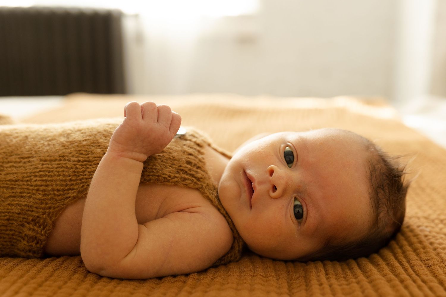 Baby lying on textured brown blanket in natural lighting.