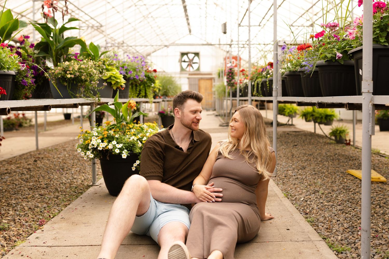 Happy couple laying on greenhouse floor sharing intimate moment among plants.