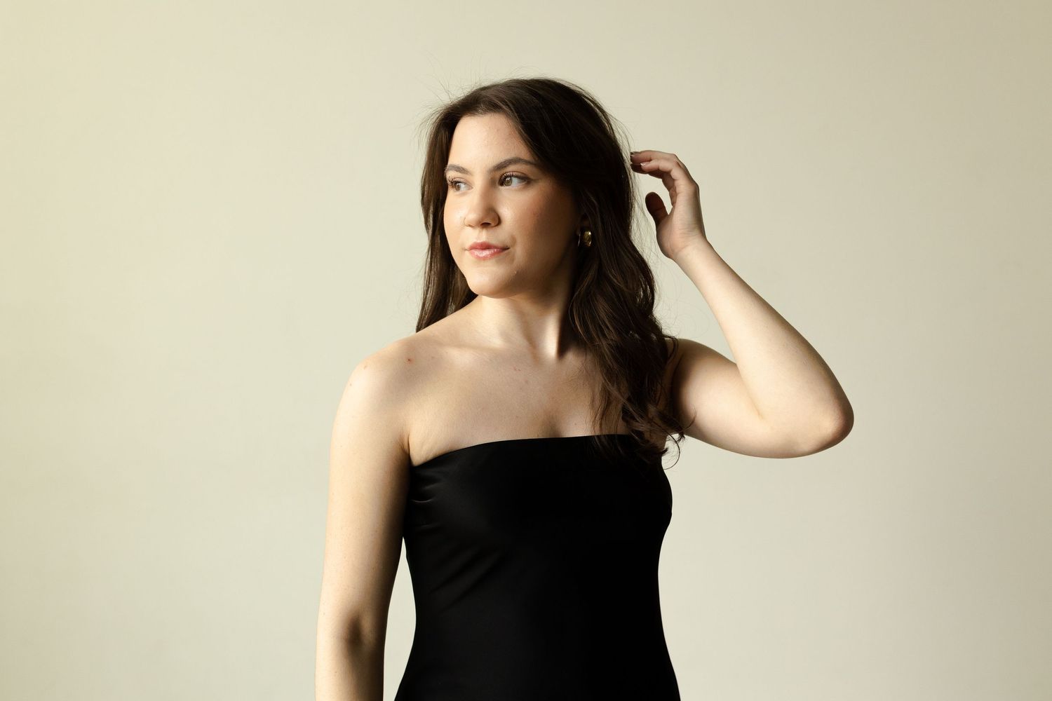 Elegant studio portrait in black strapless dress against neutral background.