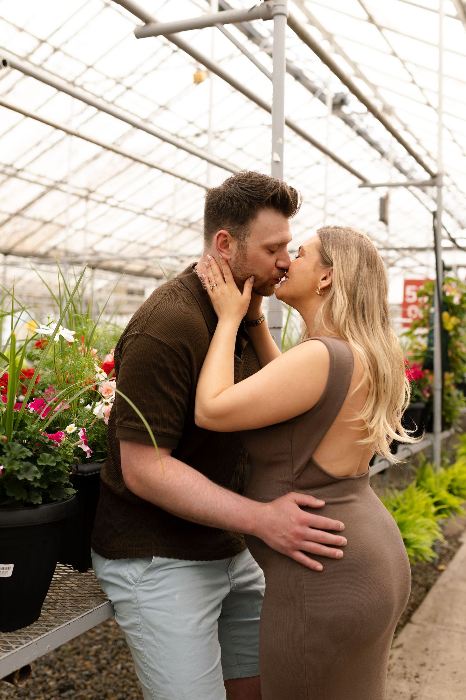 Sweet maternity moment captured in greenhouse with natural lighting and floral backdrop.