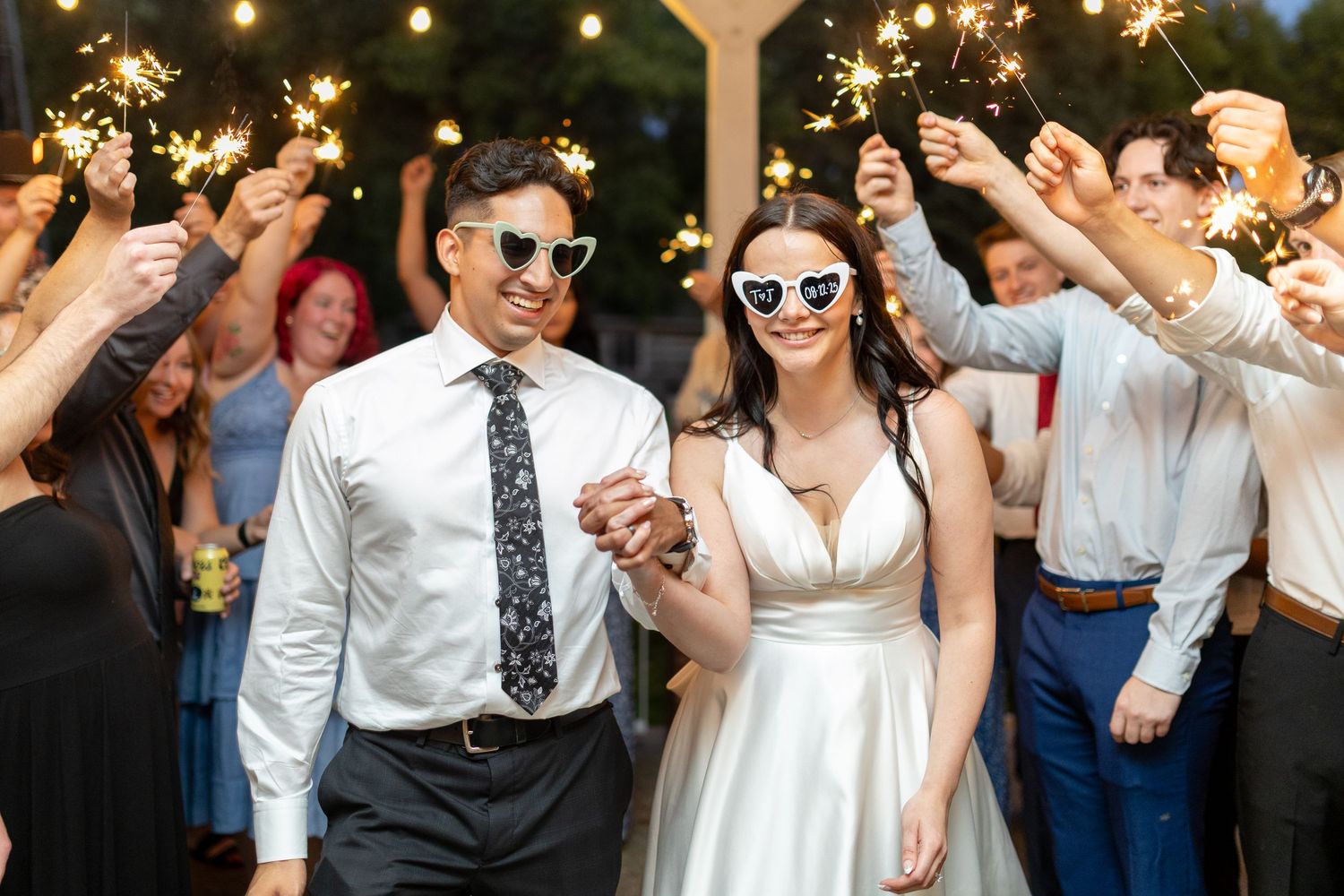 Wedding guests dance and celebrate with sparklers during an outdoor evening reception celebration.