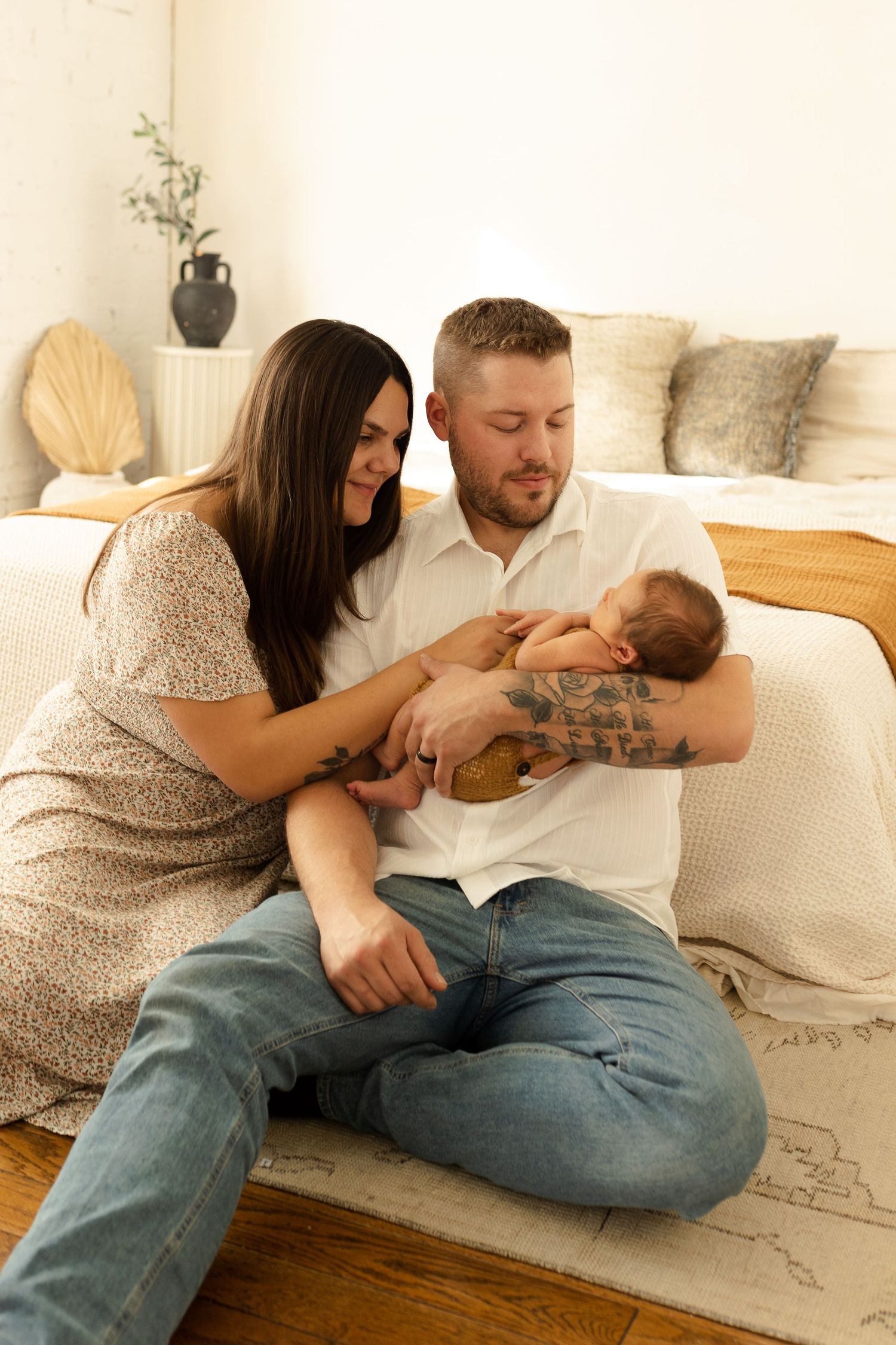 Parents share playful moments with their infant on a white couch in a minimalist living room setting.