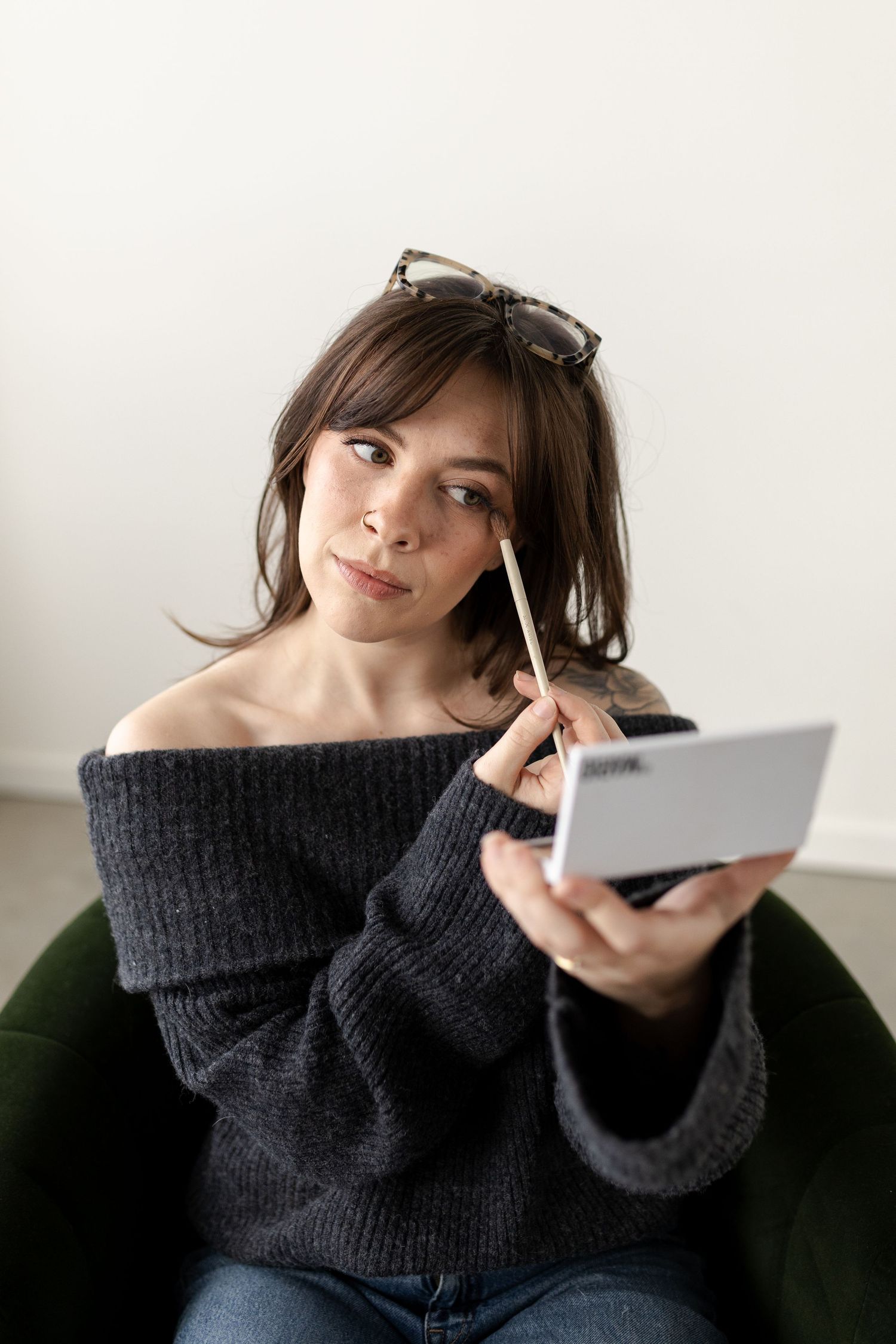 A person in a cozy dark sweater poses playfully with a white mobile device against a light background.