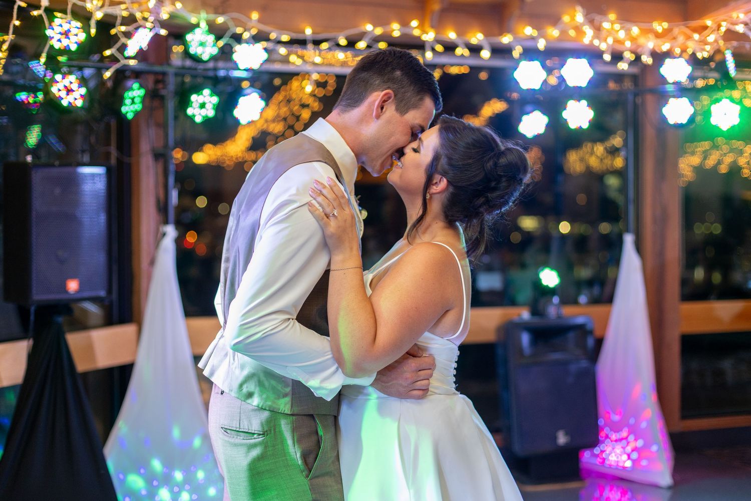 Couple dancing under colorful party lights during evening wedding reception.