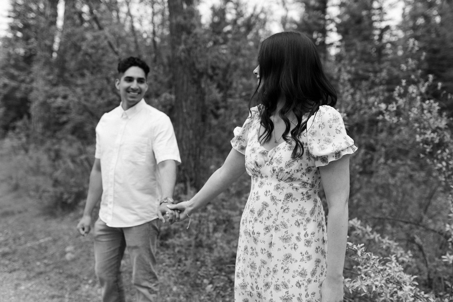 Candid black and white photo of a couple walking through a wooded area.
