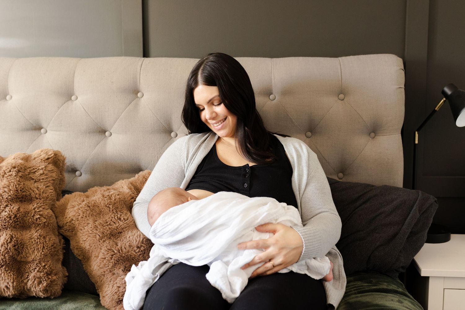 A tender moment captured in a living room as a woman cradles a swaddled infant on a tufted couch.