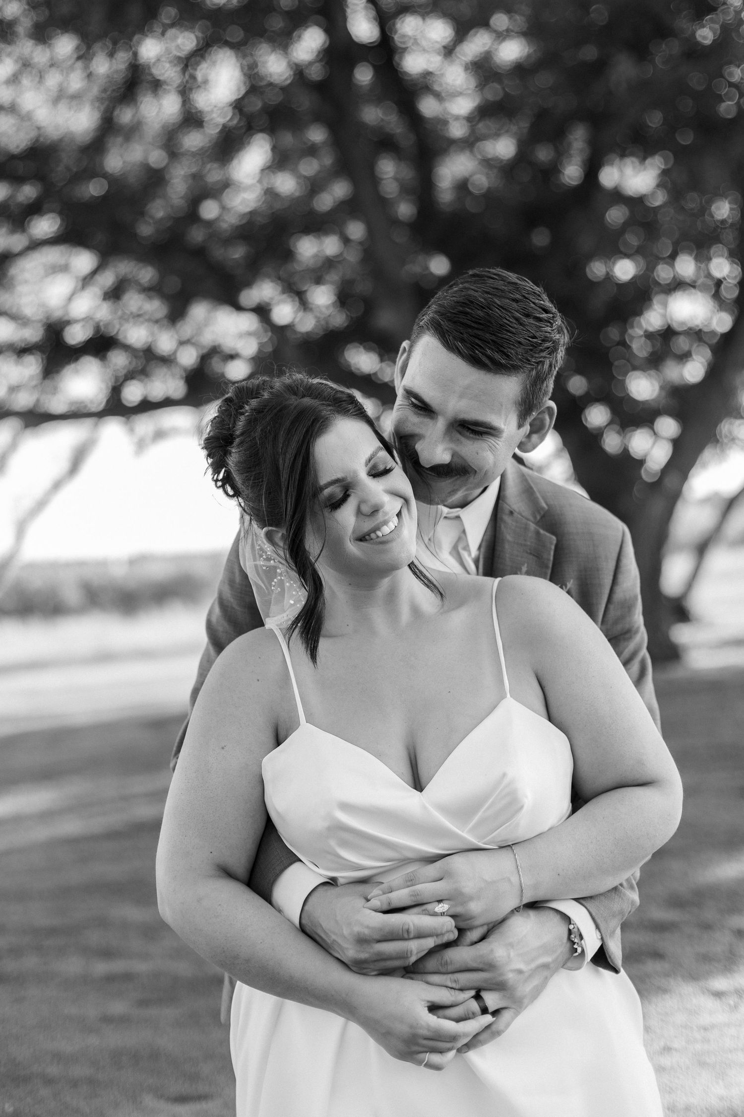 A tender embrace between newlyweds in a black and white outdoor portrait.