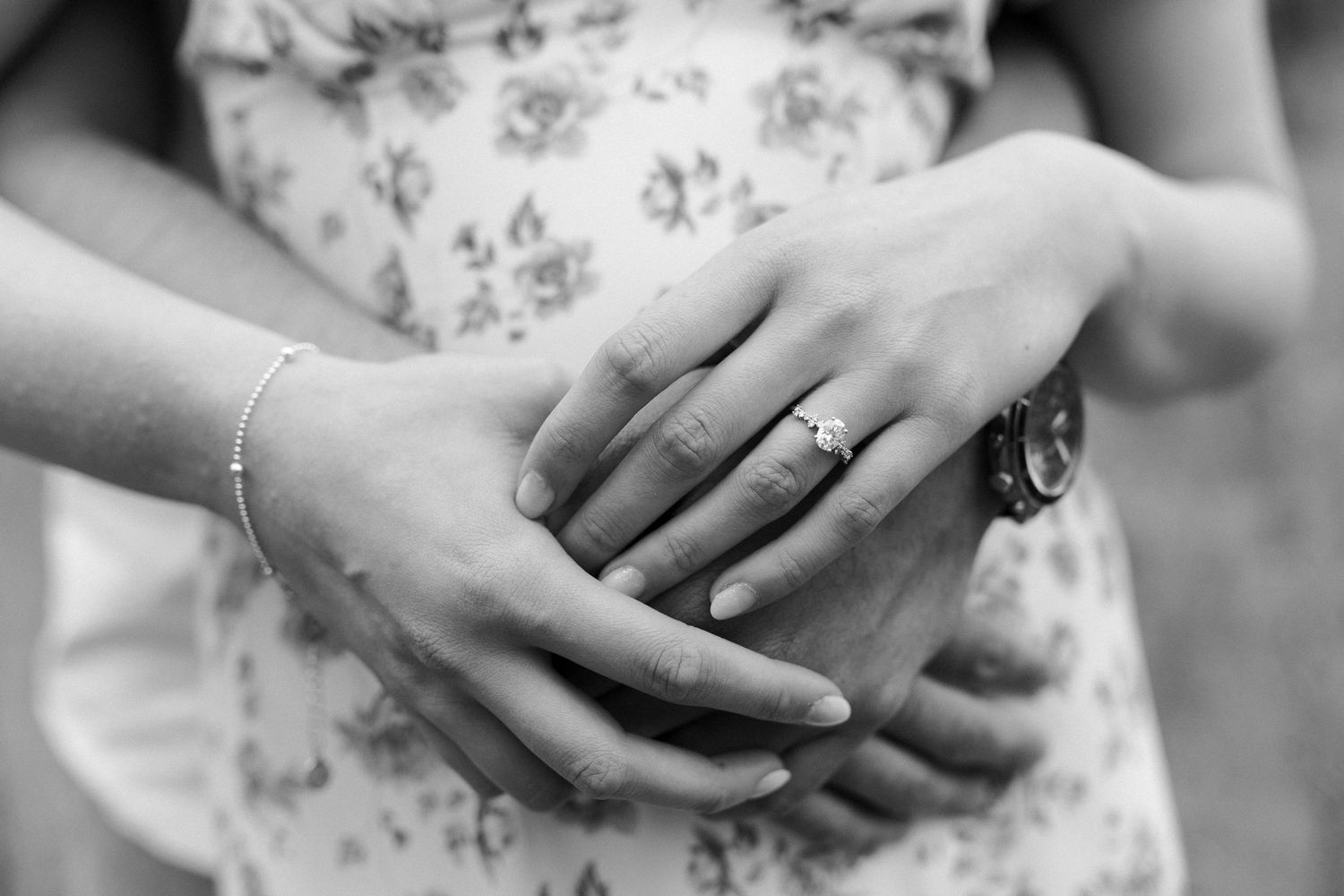 Close-up of hands showing engagement ring against floral dress fabric.