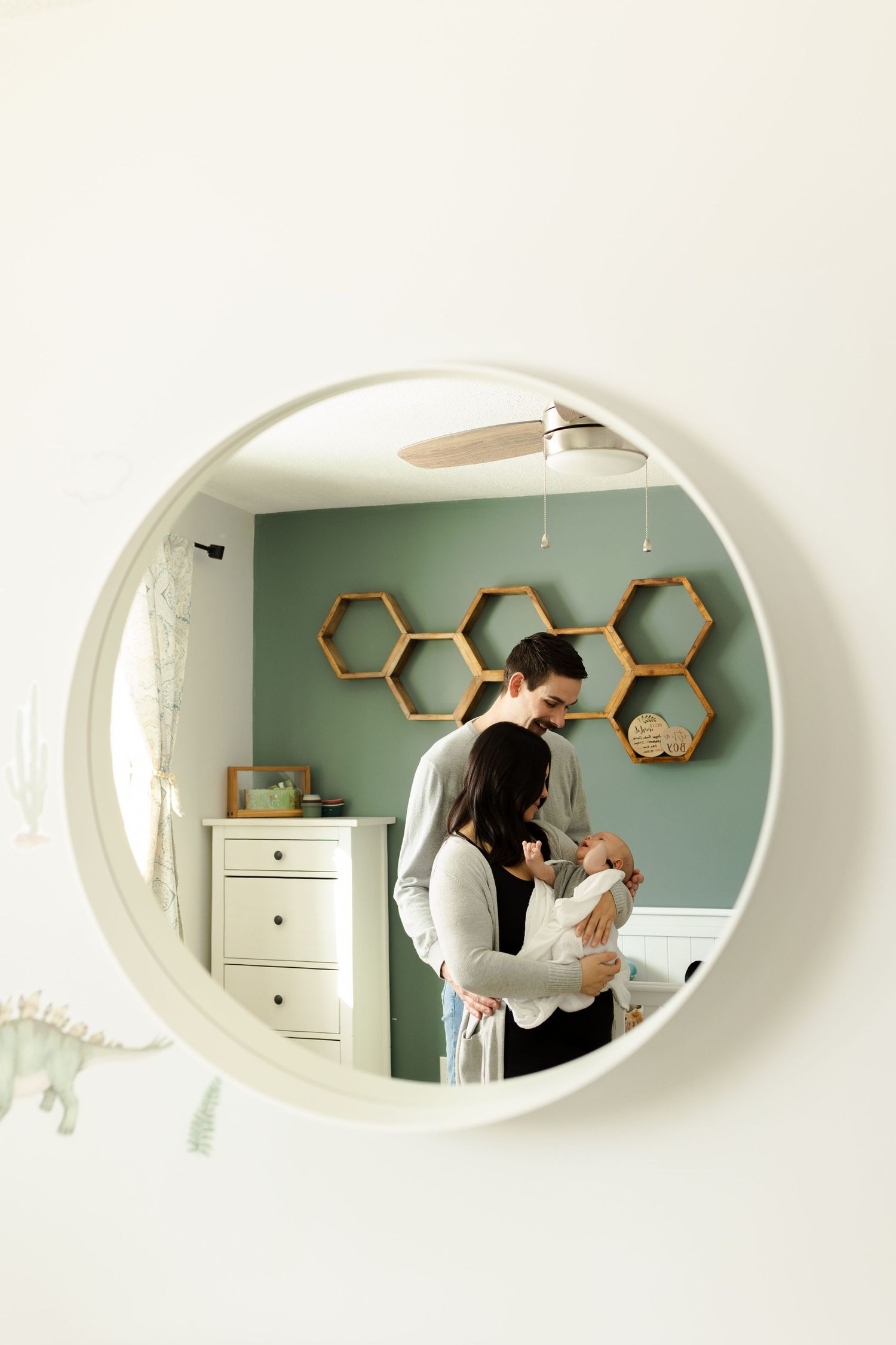 Family portrait session reflected in an oval mirror with hexagonal shelves on mint green wall.