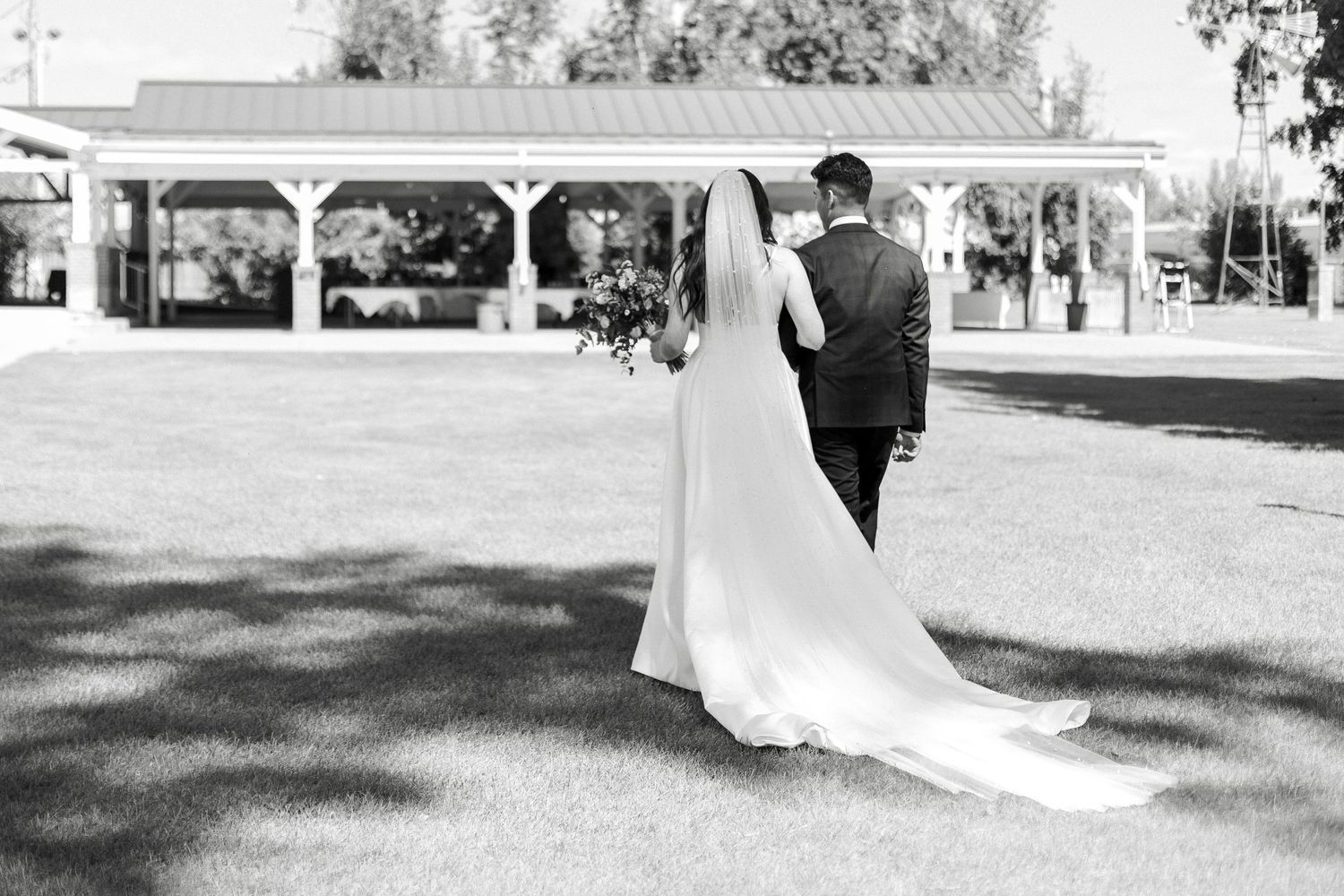 A bride and groom walk together outdoors in a park setting during their wedding photo session.