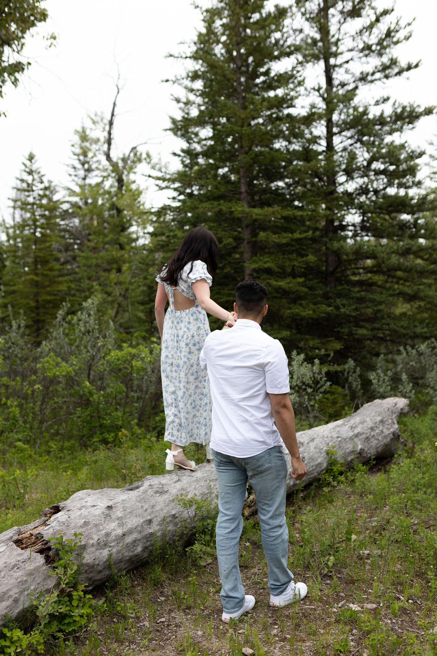 Two people balancing on a fallen log in a forest setting.