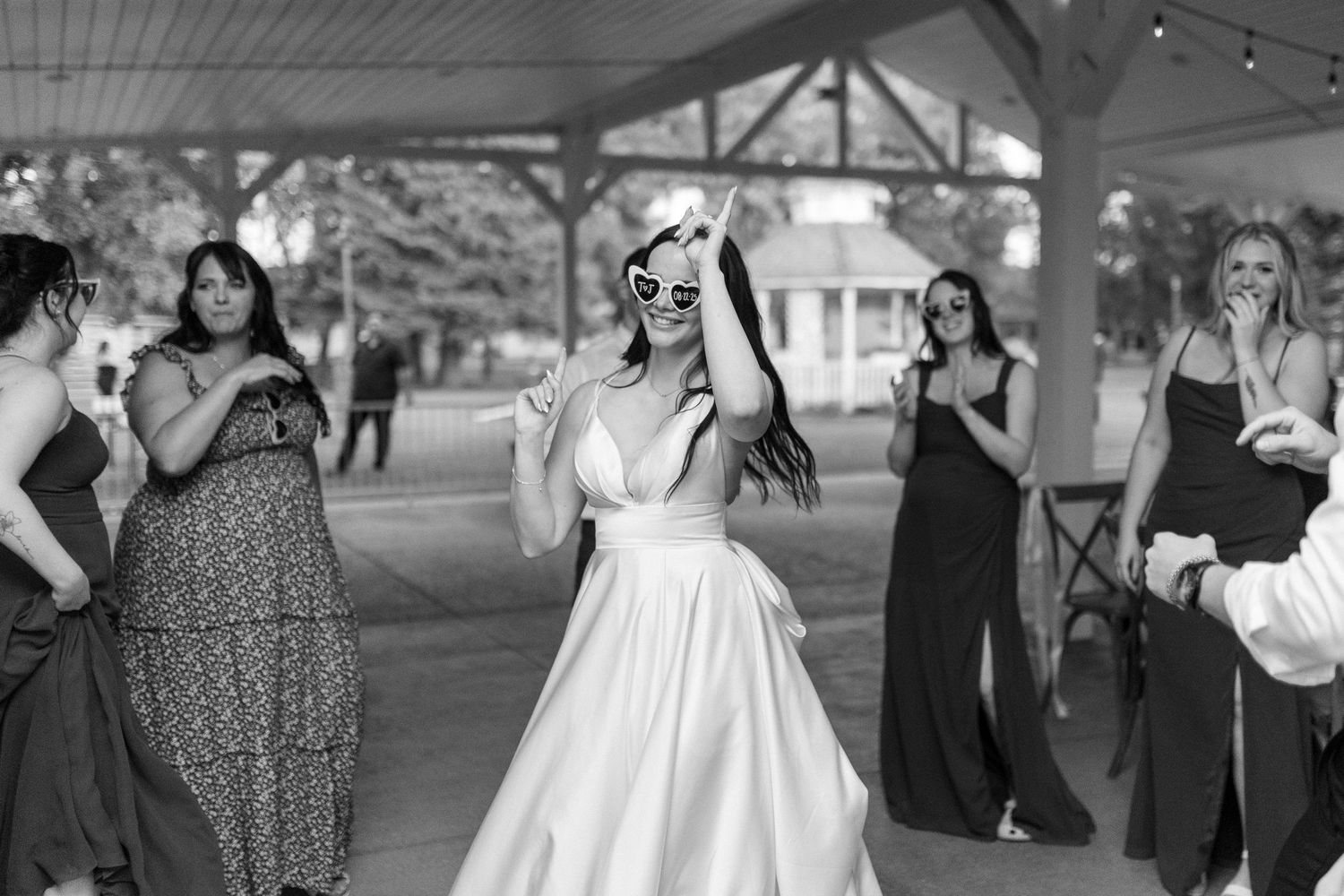 Wedding party members in formal attire dance and celebrate at an outdoor reception.