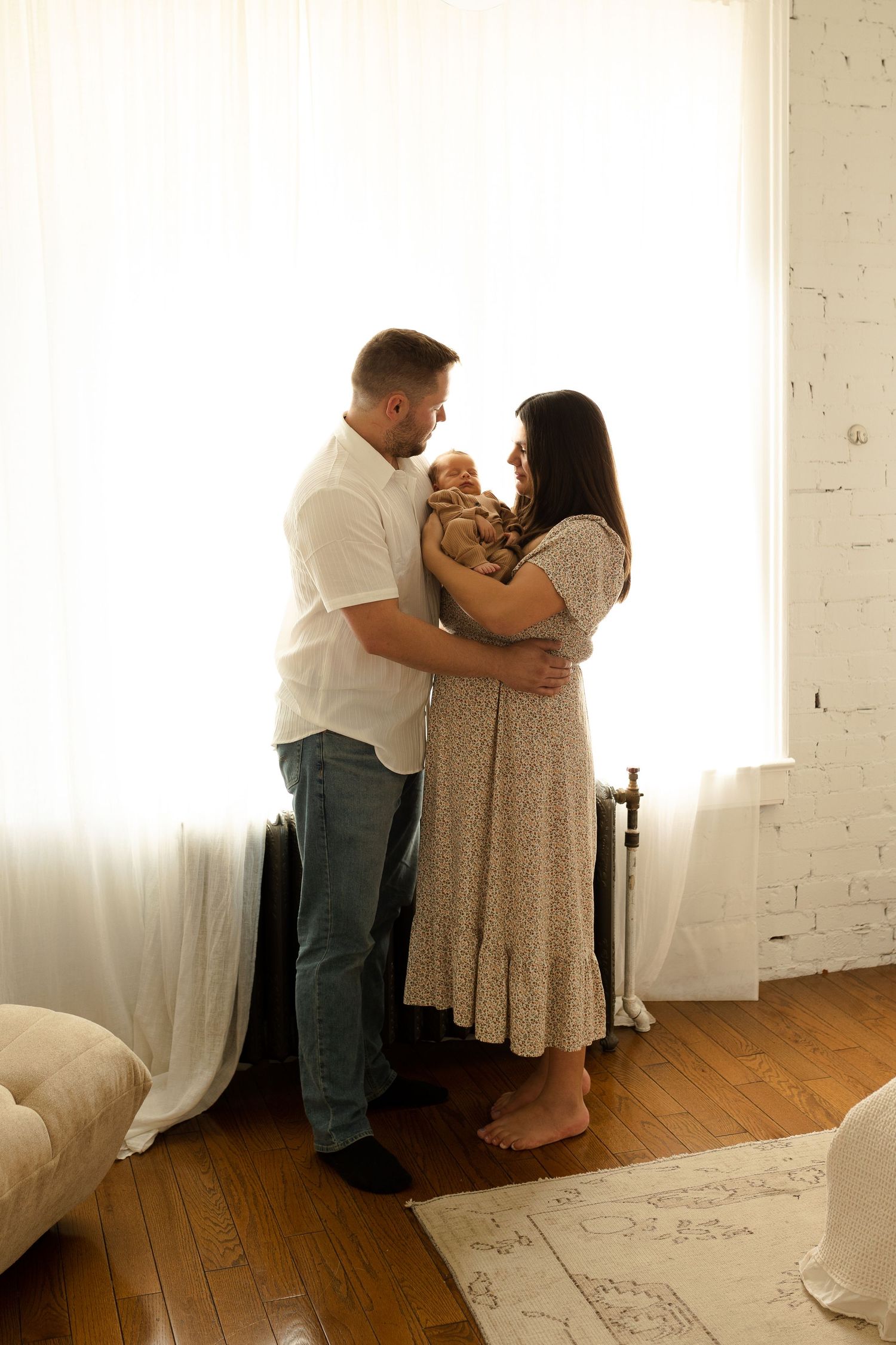 A couple shares an intimate moment dancing together in a bright, sunlit studio space with wooden floors.