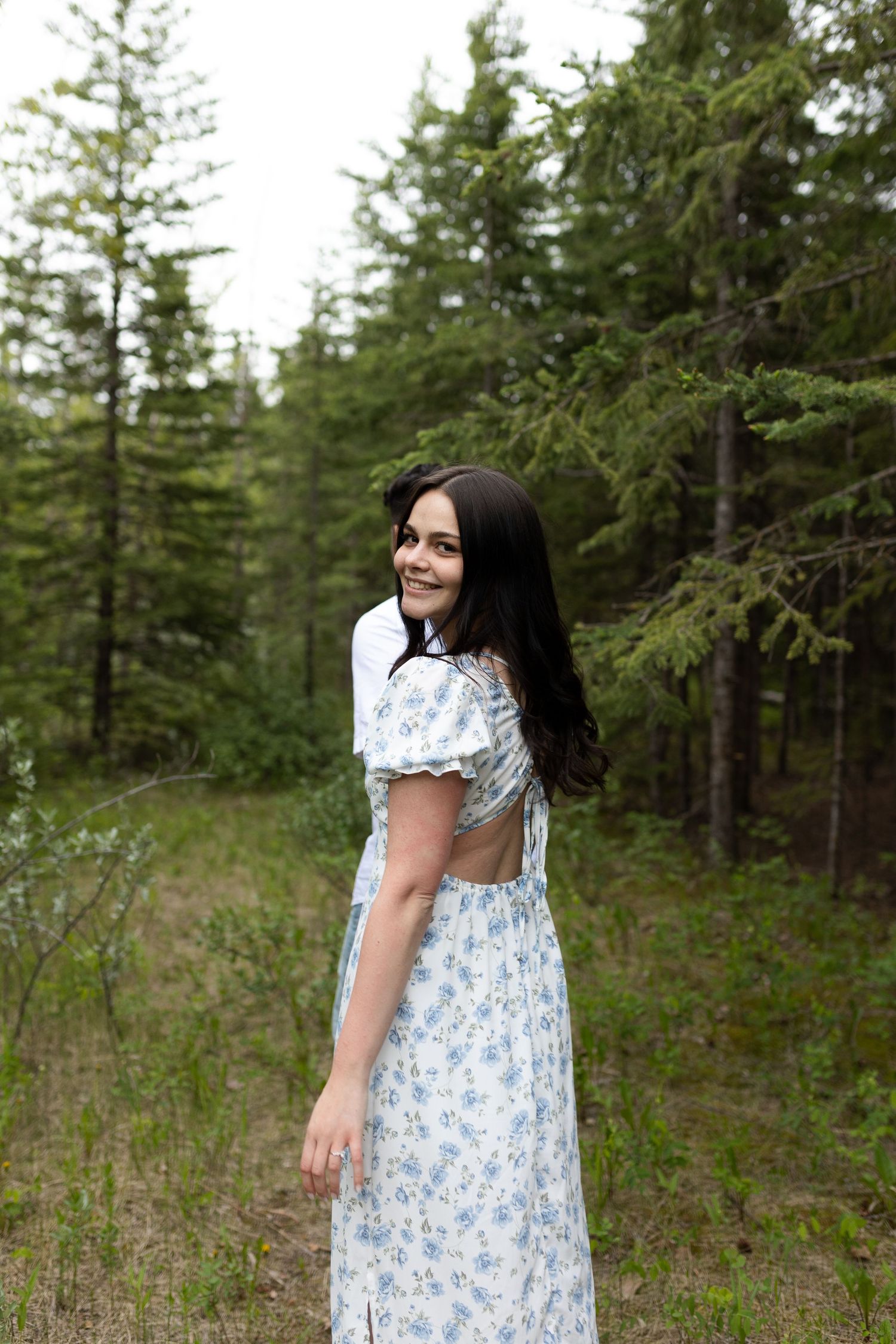 Woman in a blue floral dress poses in a forest clearing.