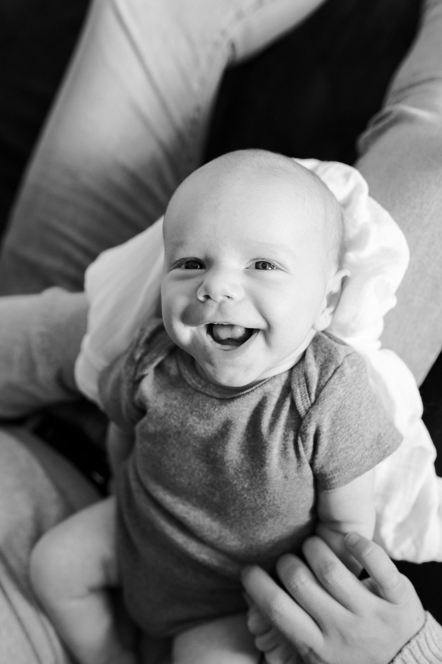 Black and white photo series of a baby wearing a gray onesie smiling with joy.