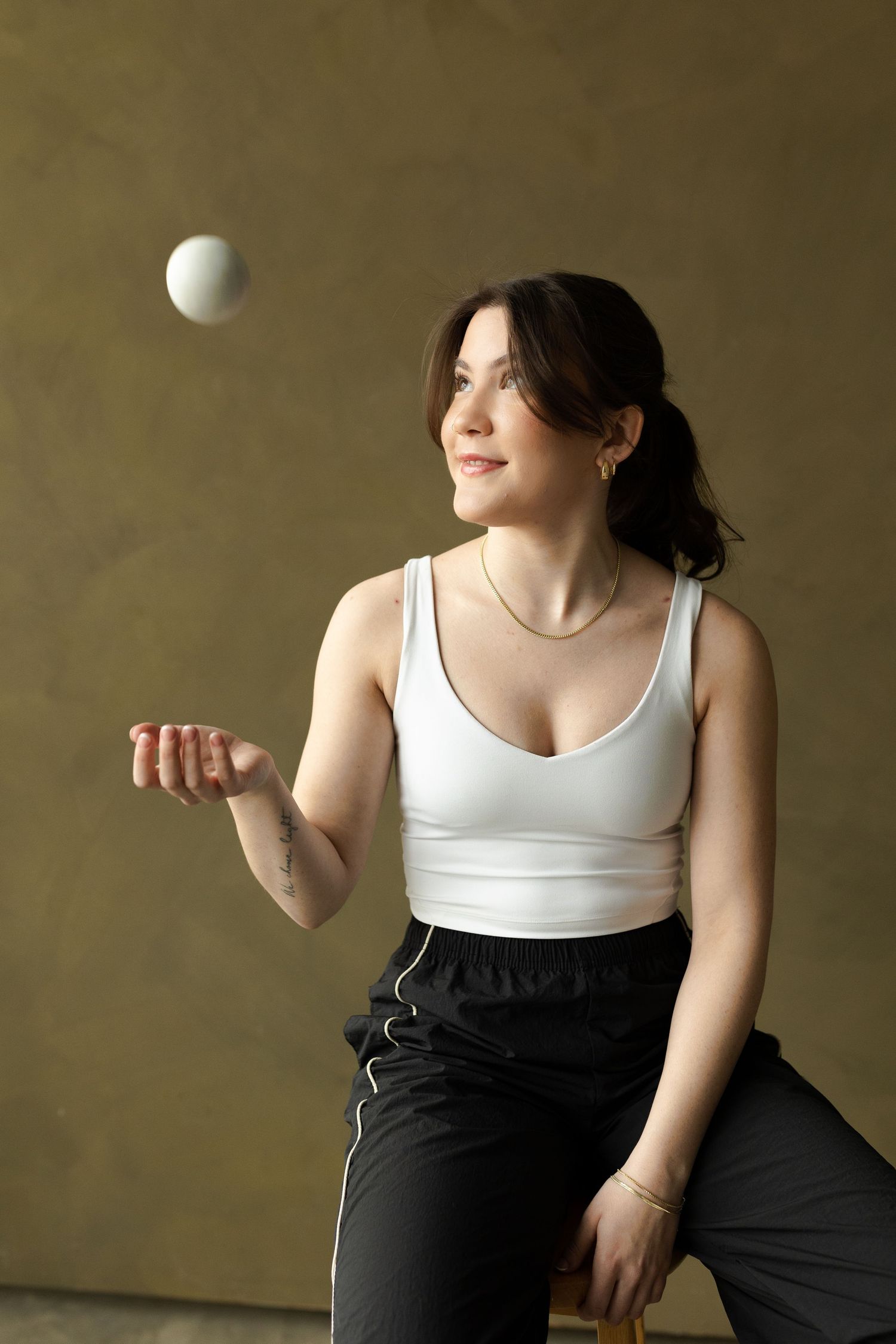 A series of four connected images showing someone in a white tank top and black pants juggling a white ball against a brown wall.