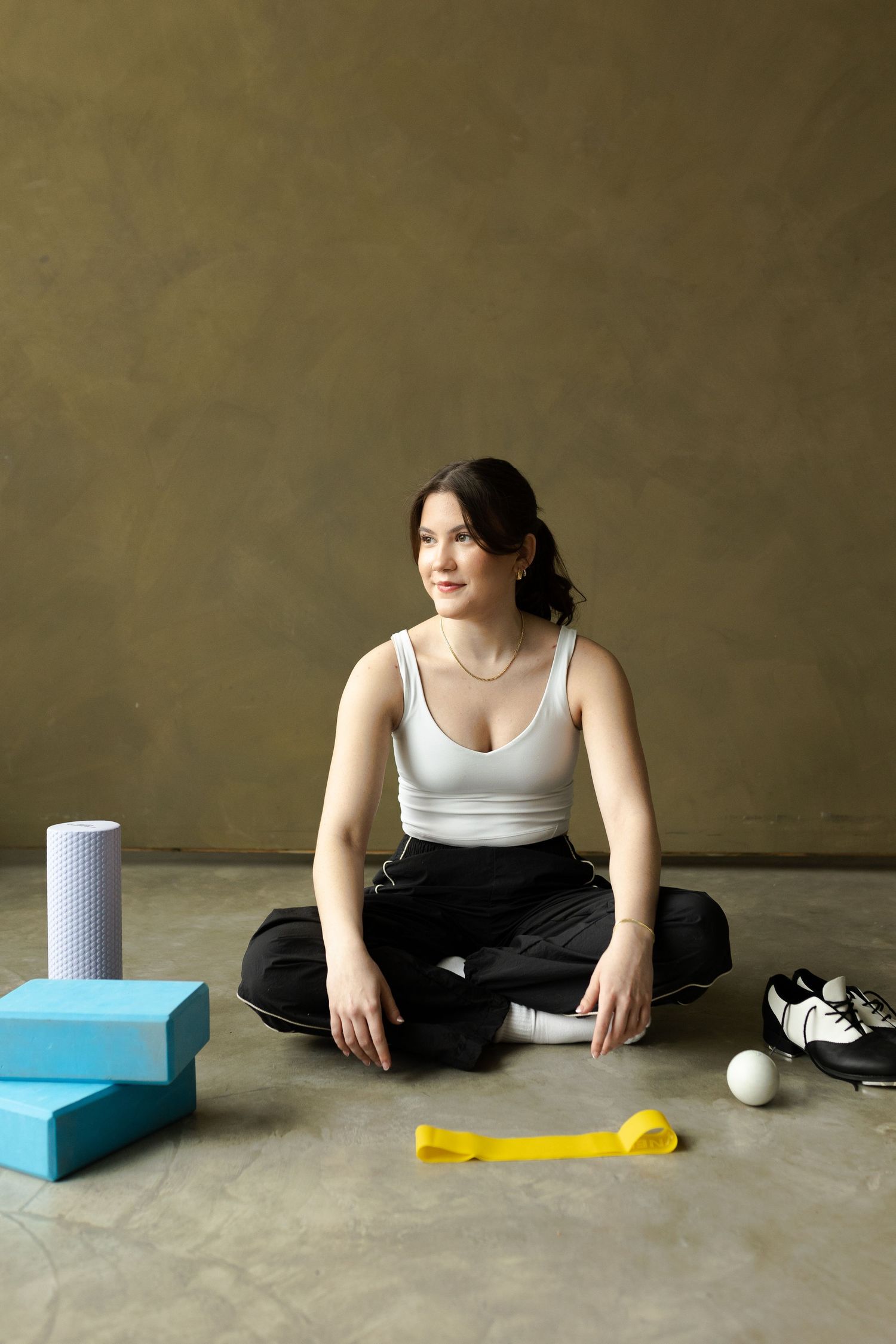 A person in workout attire sits cross-legged on the floor with exercise equipment including yoga blocks and a dumbbell nearby.