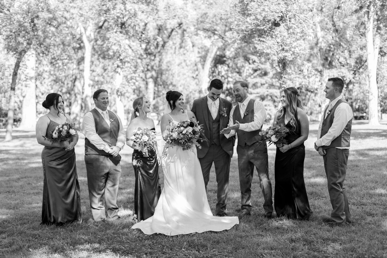 Wedding party gathered outdoors under trees in black and white photography.