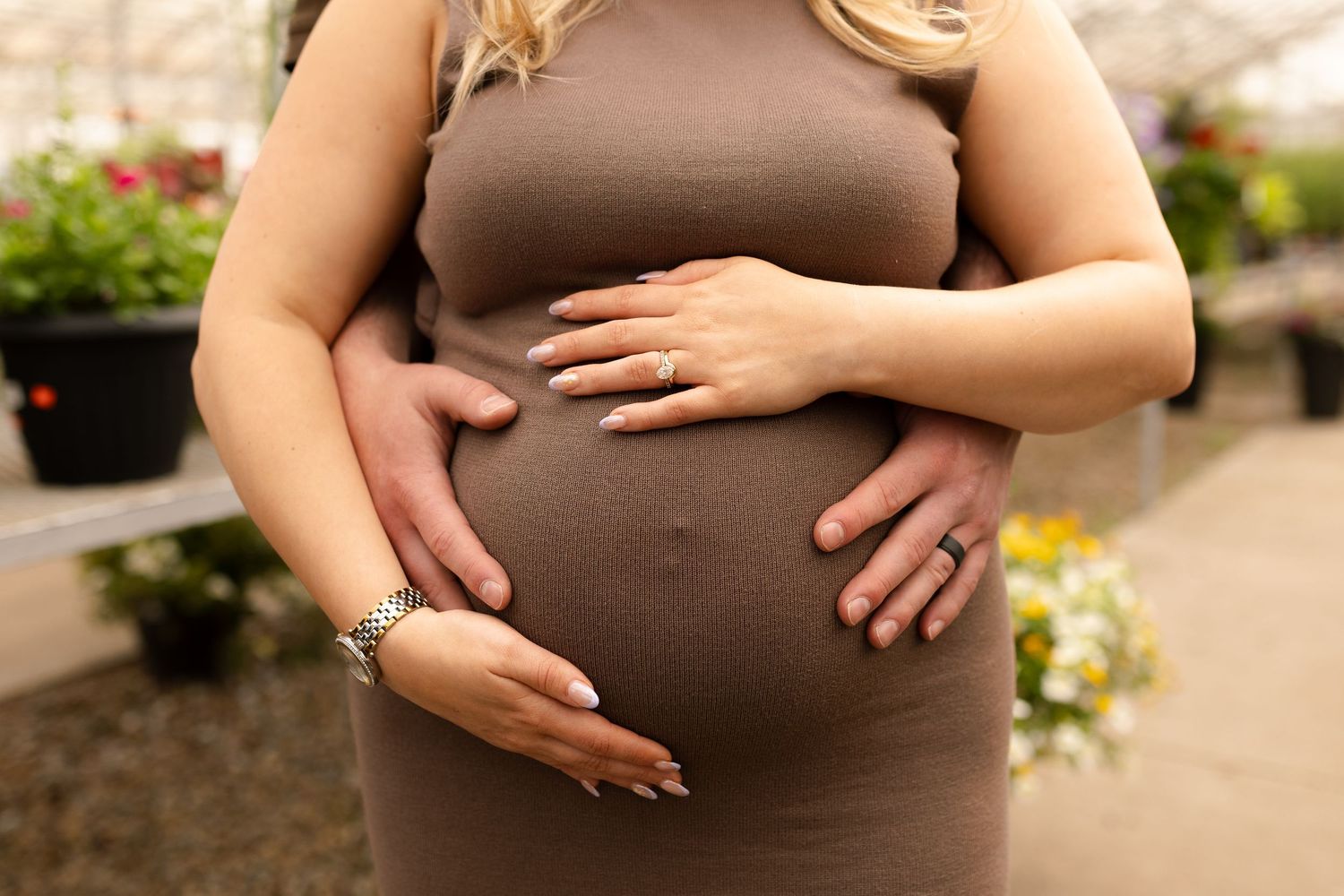 Close up of hands tenderly cradling pregnant belly in brown dress.