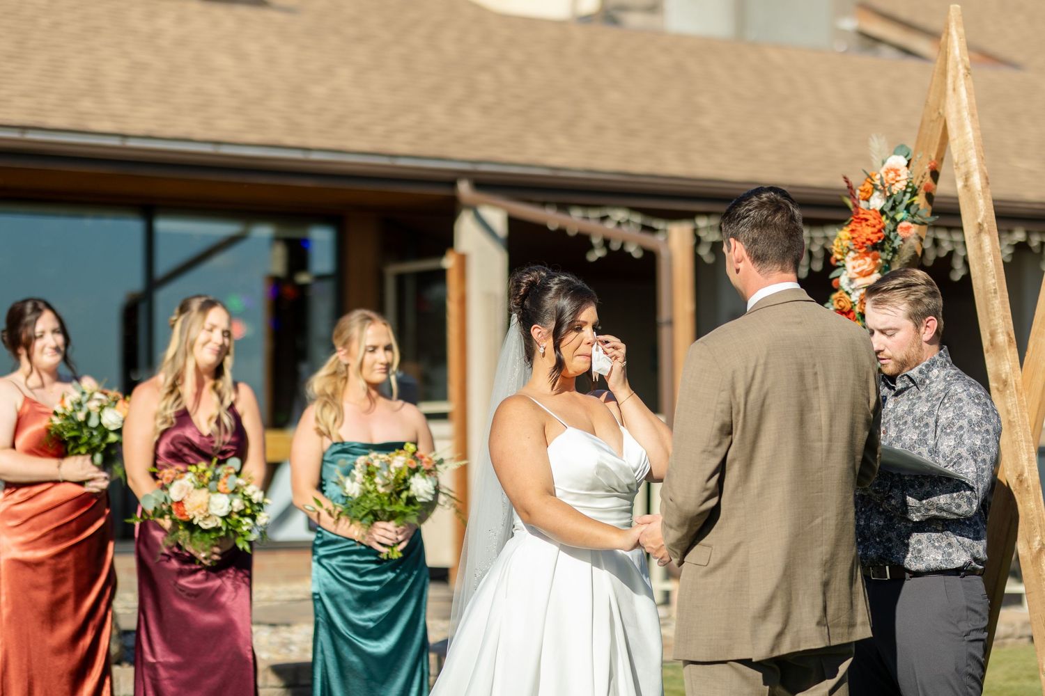 Wedding party members pose together outdoors with bridesmaids in jewel-toned dresses.