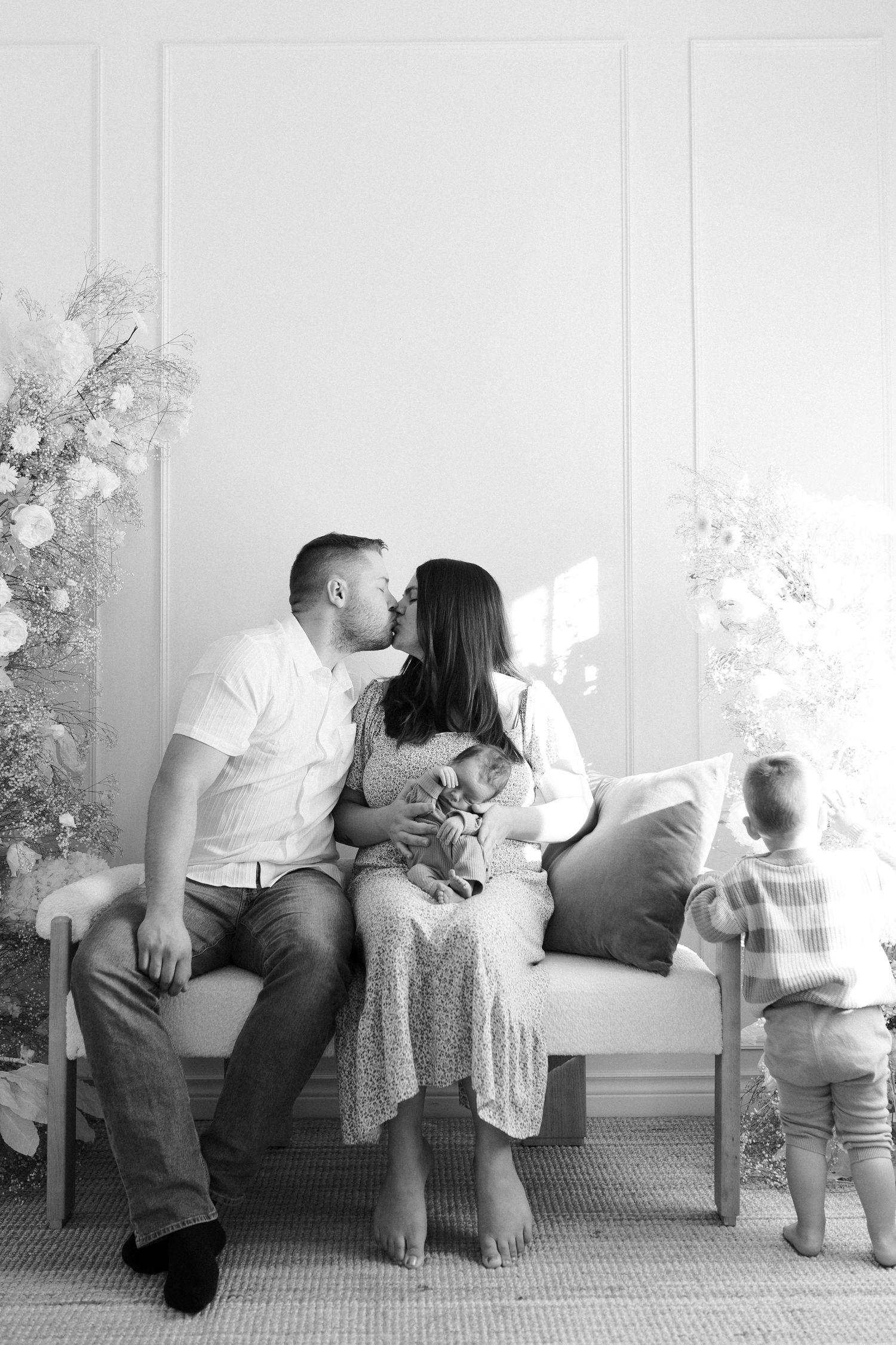 Black and white photo series showing tender family moments on a couch by a window.