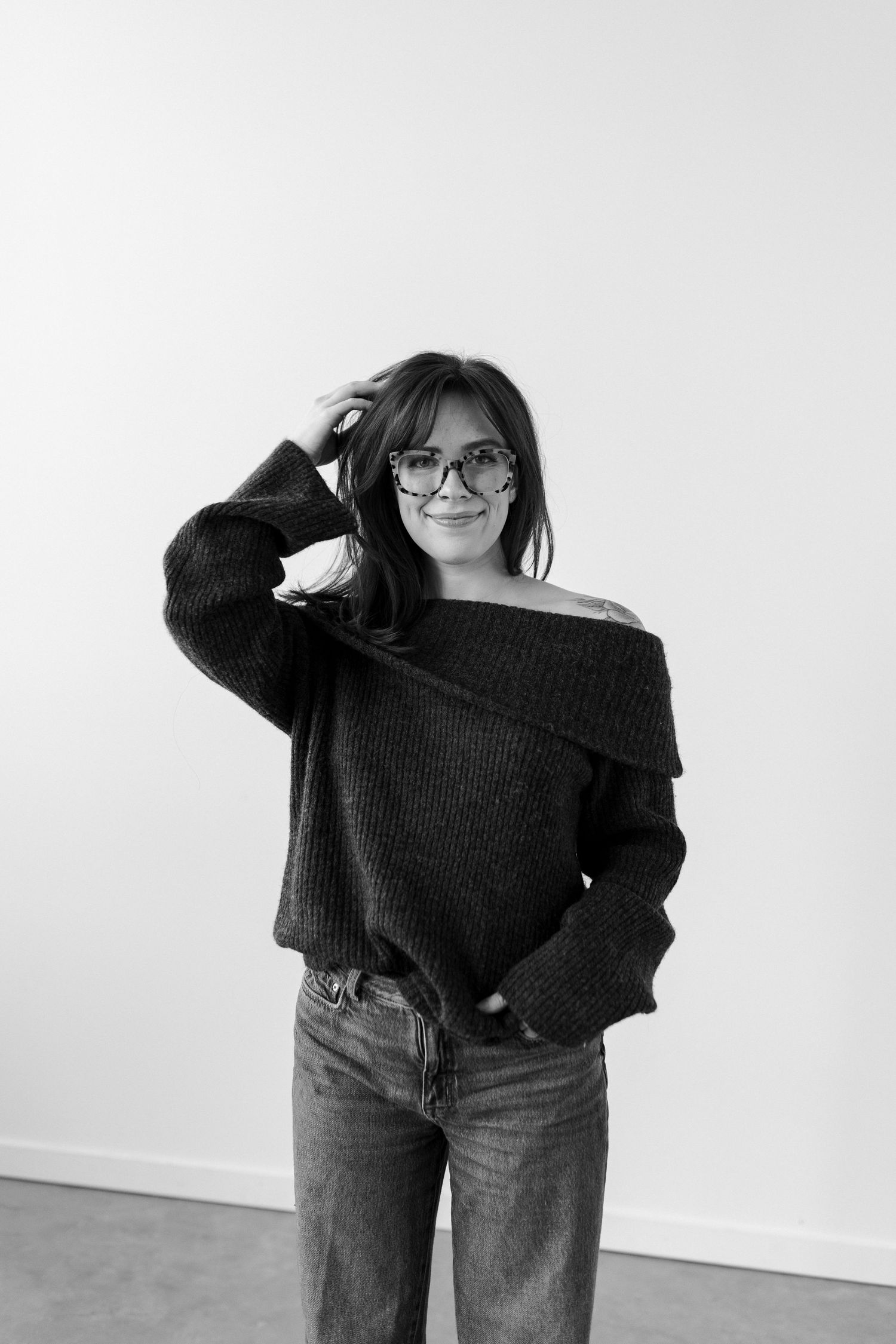 Black and white photo series showing someone in an oversized sweater and jeans posing playfully against a white wall.