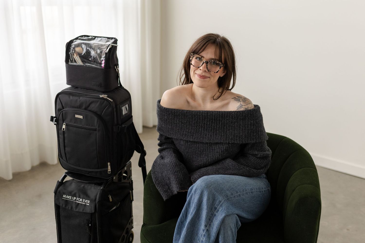 A person sitting in a black office chair with camera equipment and gear bags visible in the background.