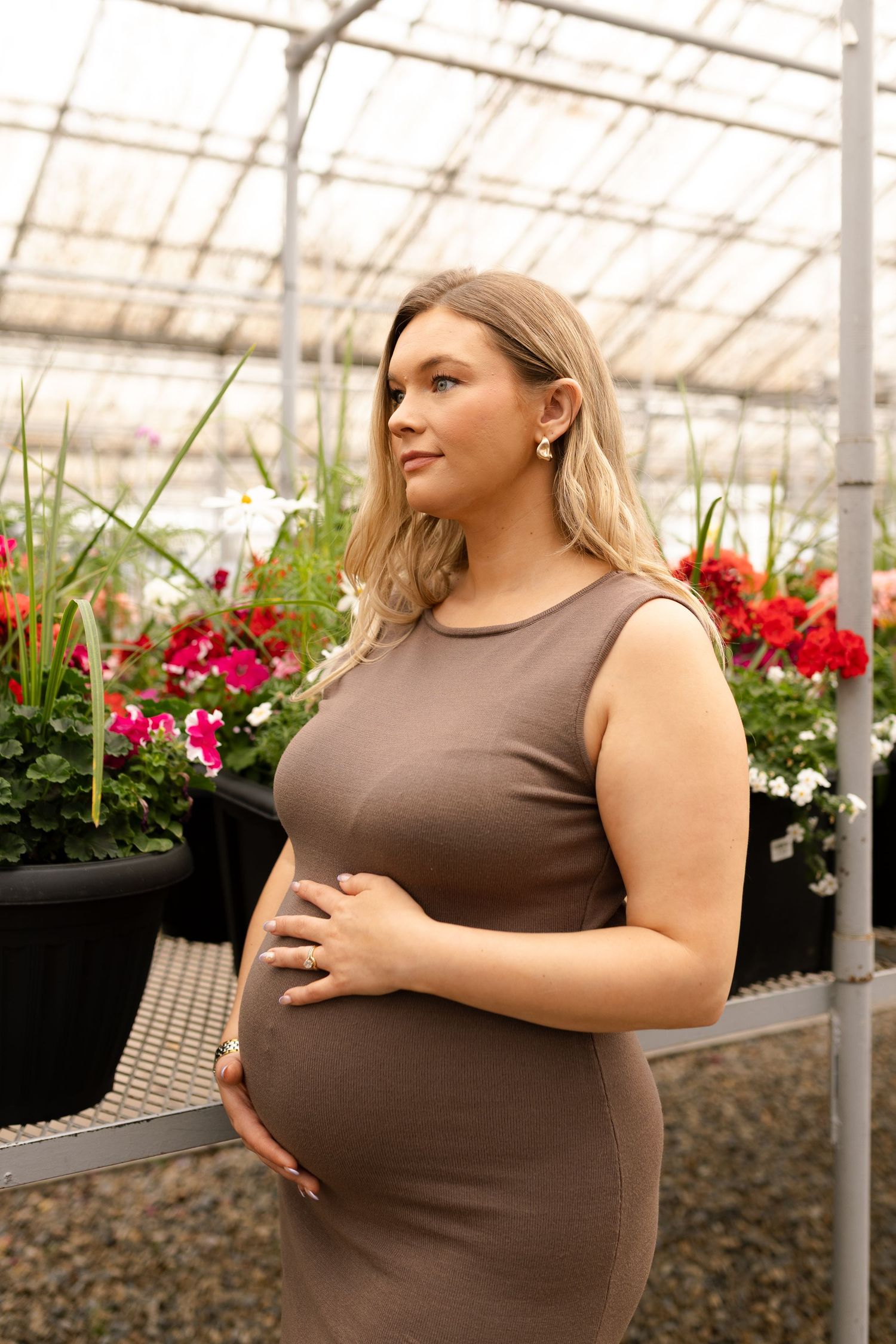 Serene maternity portrait in greenhouse showing expectant mother in brown dress among plants.