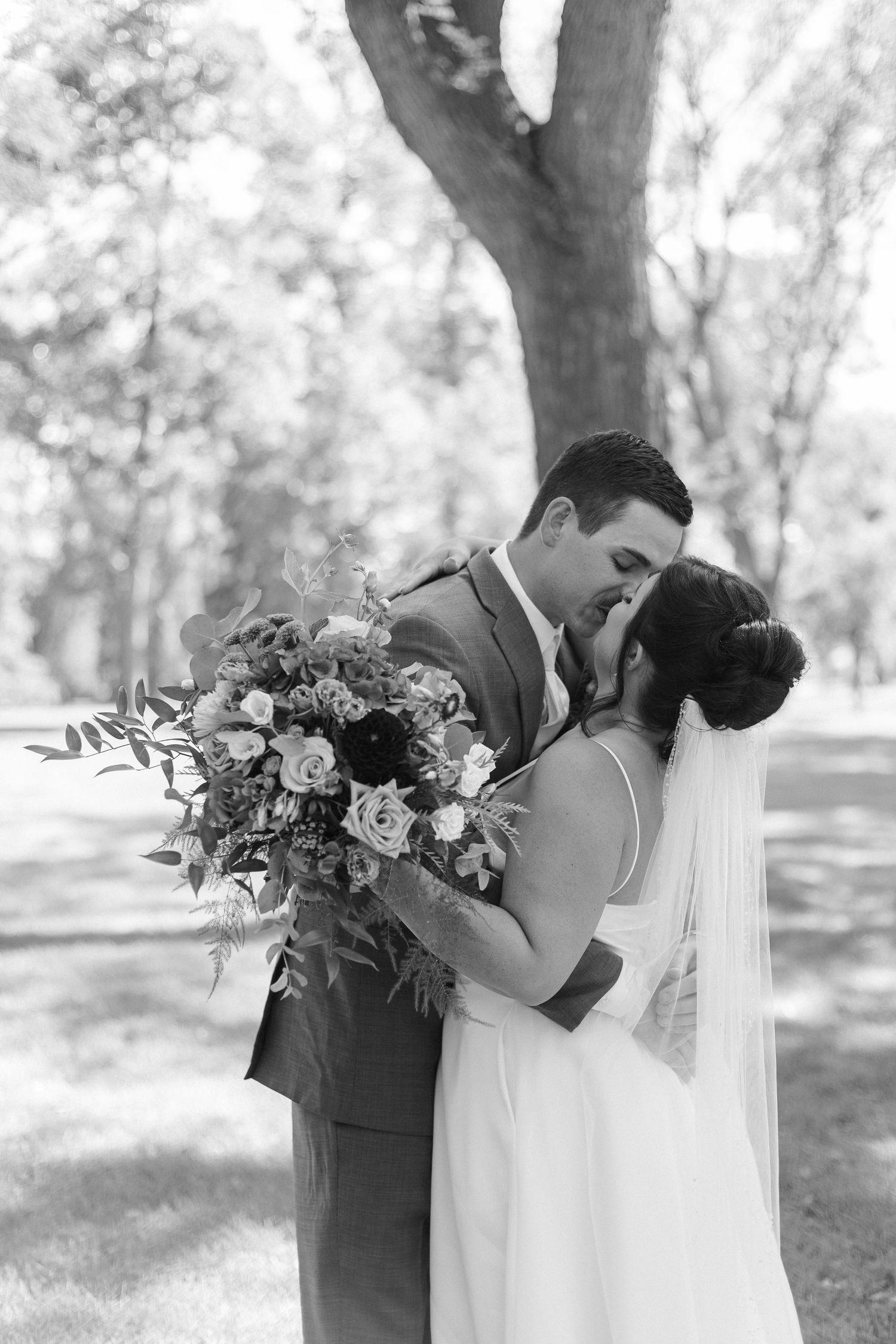 A romantic wedding couple shares intimate moments in a wooded setting with beautiful floral bouquets.